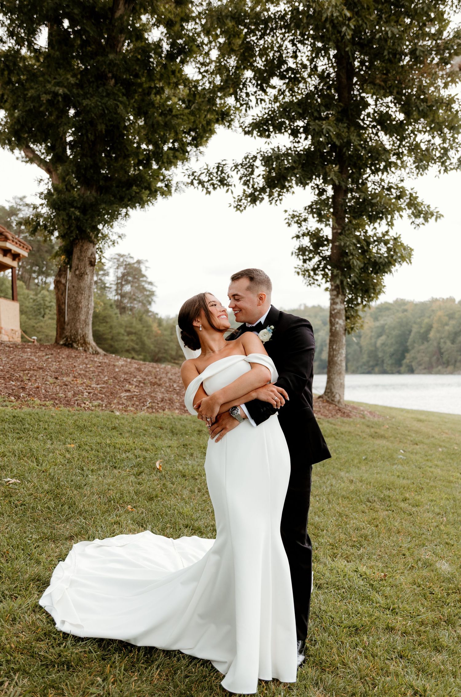 Joyous couple joyfully embrace with a soft glowy lake behind them. smiling and laughing as he pulls he back for a kiss