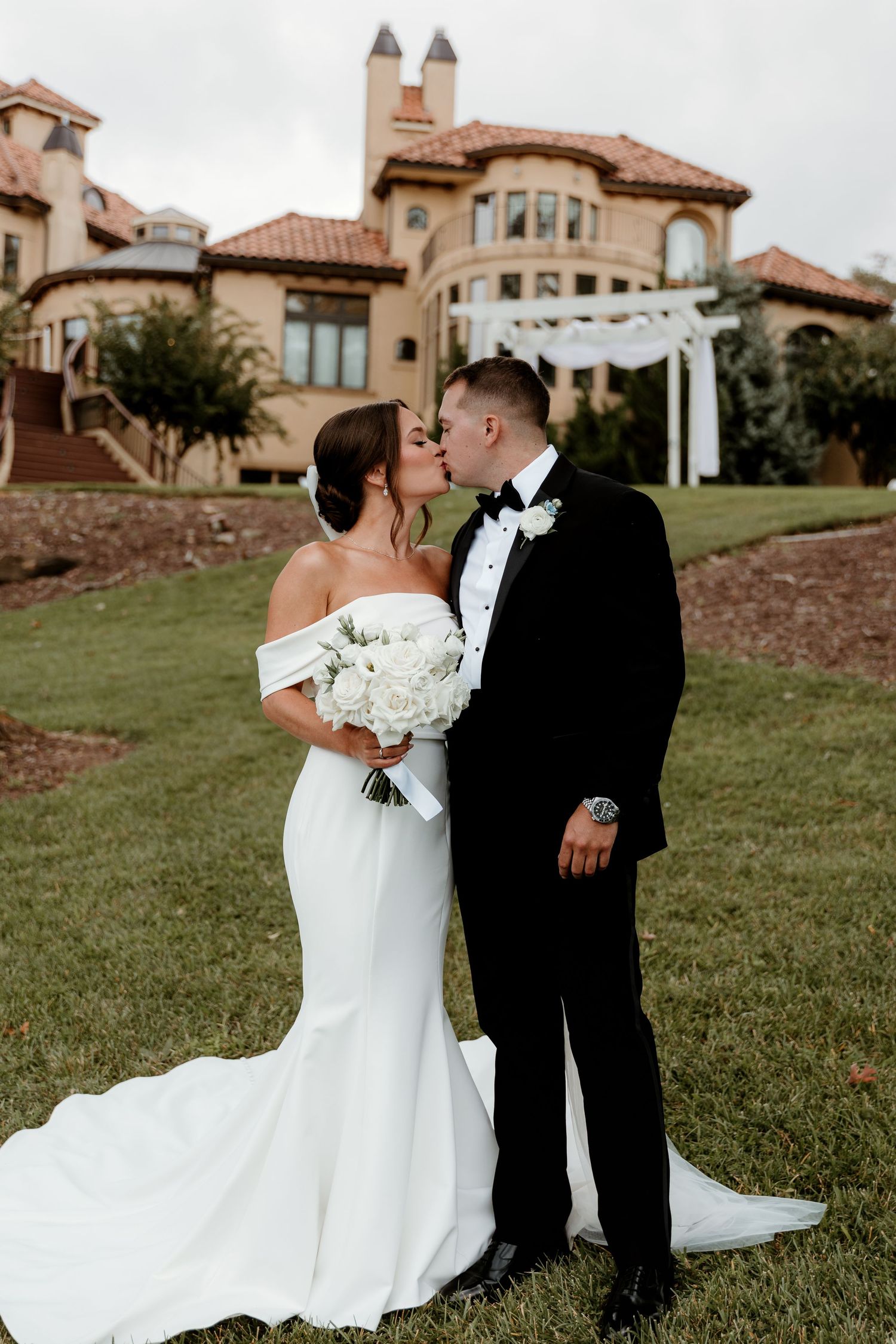 Mallory and brady kiss in front of the elegant Bella Collina Mansion while the bride holds her bouqute