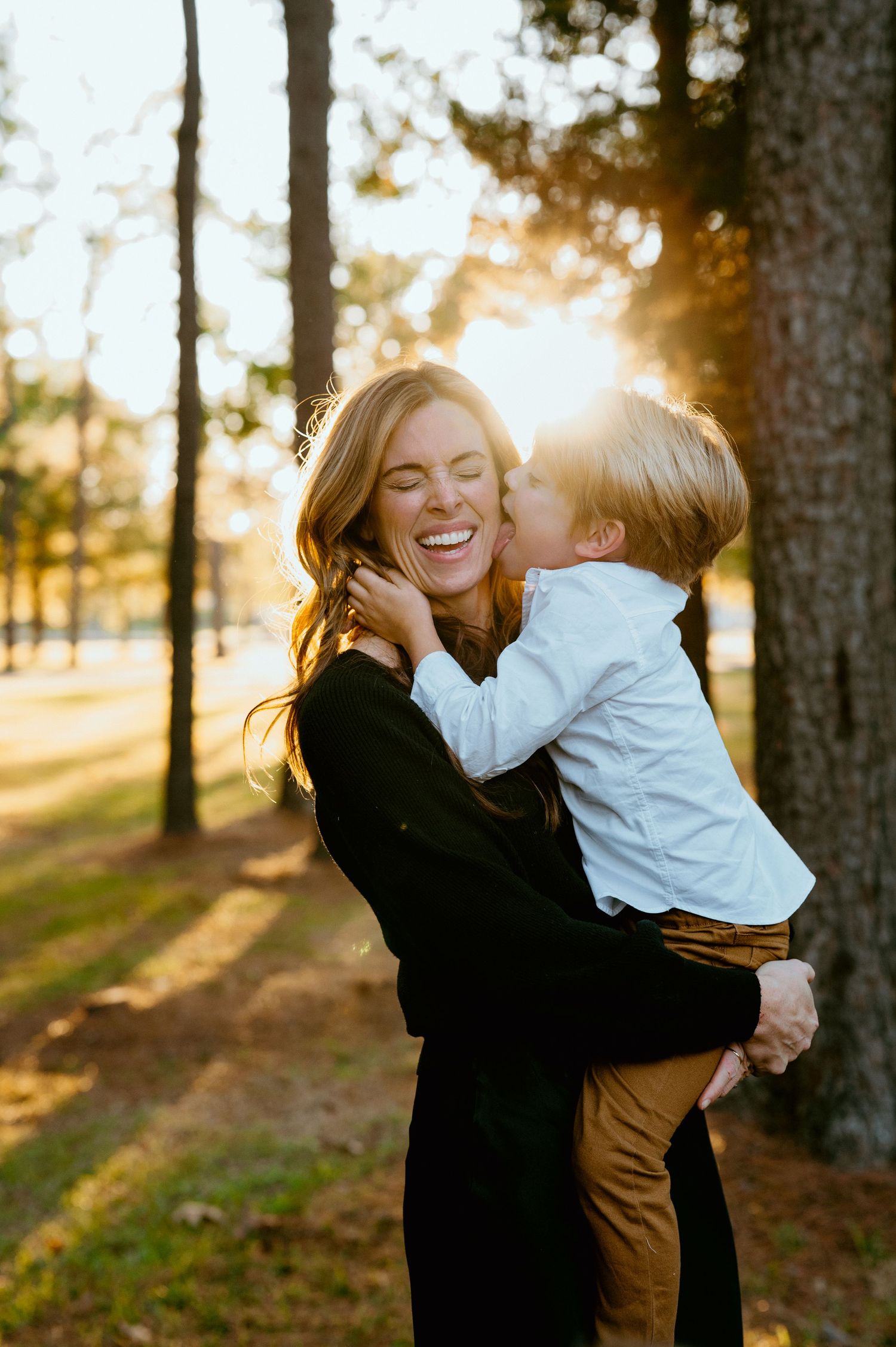 drenched in glowy sunshine, a gorgeous mother and her young son embrance and laugh as the little boy licks his mothers f