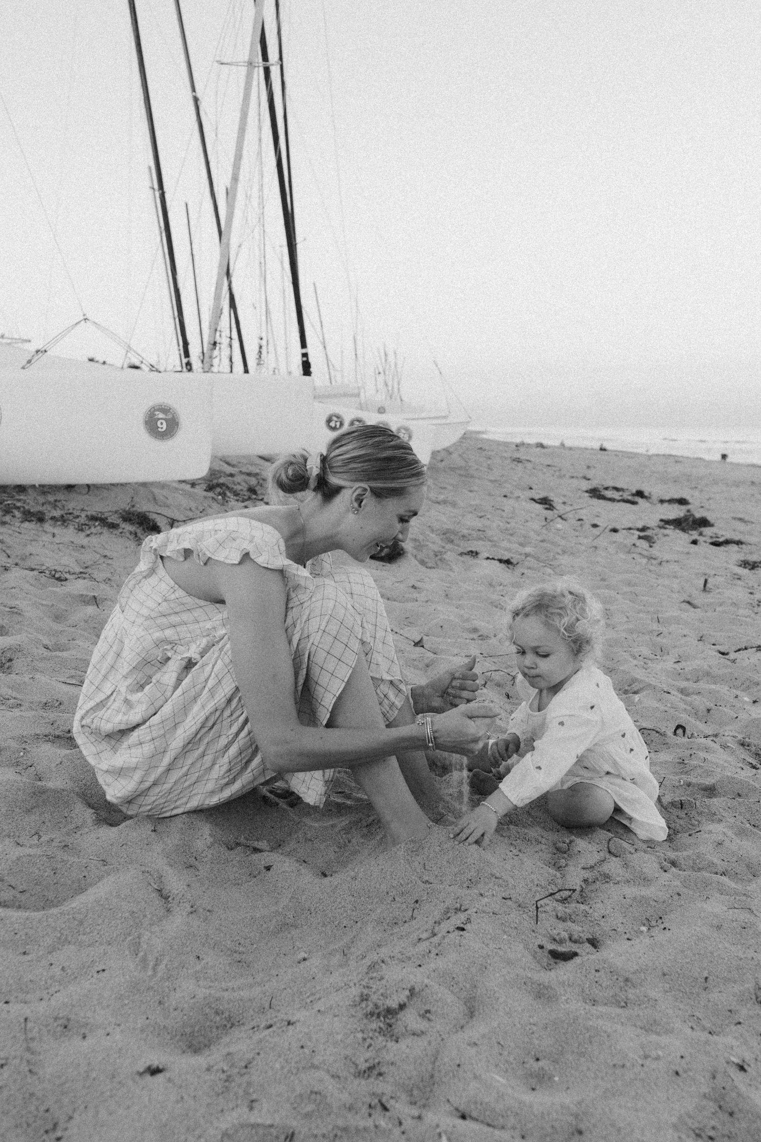 A tender moment on a sandy beach with sailboat masts visible in the background.