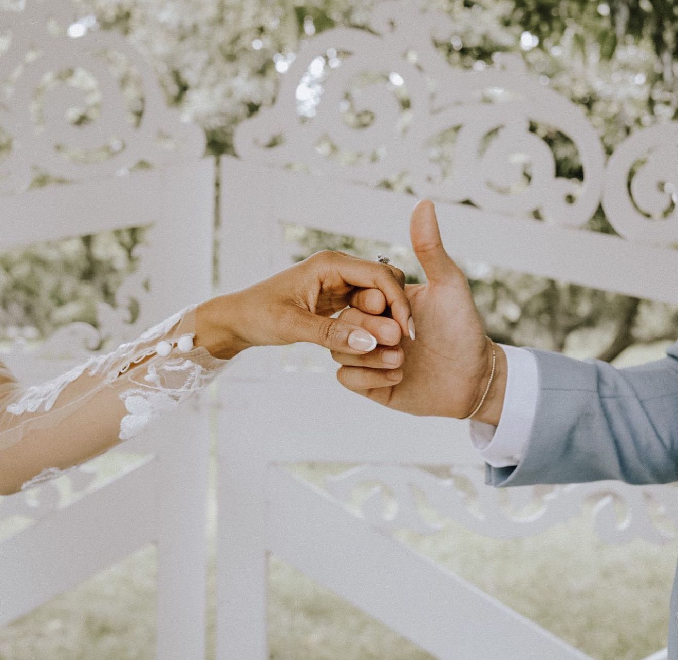 Two hands tenderly clasping in front of decorative white lattice background.