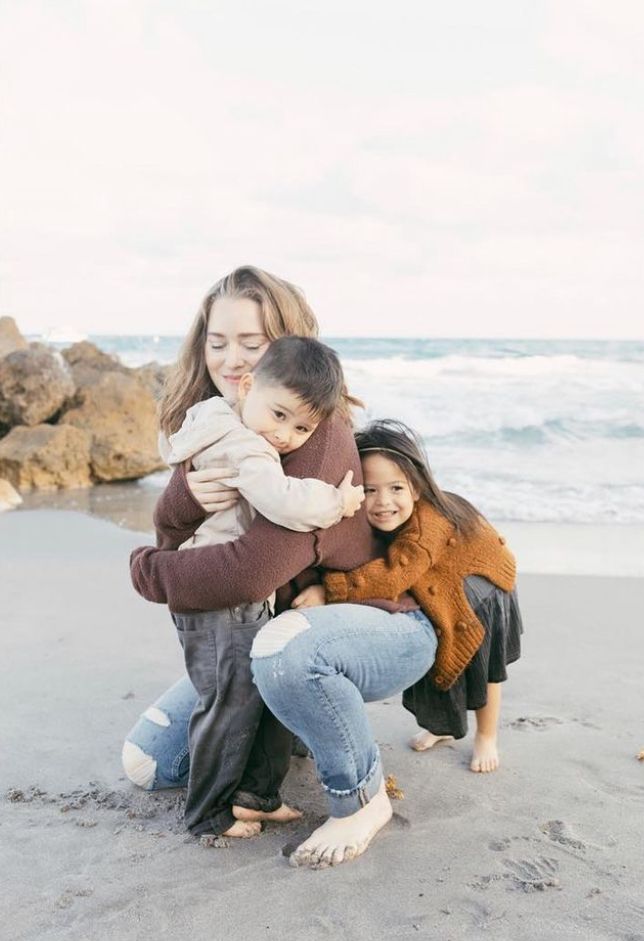 A heartwarming family moment captured on a rocky beach shore with crashing waves in the background.