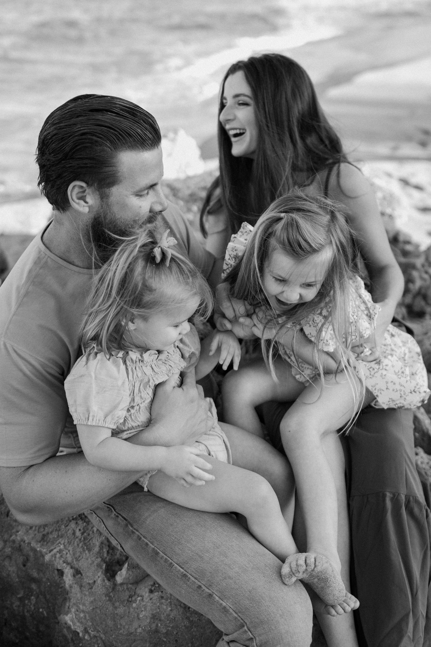 Family sharing joyful moments together while sitting on coastal rocks at sunset.
