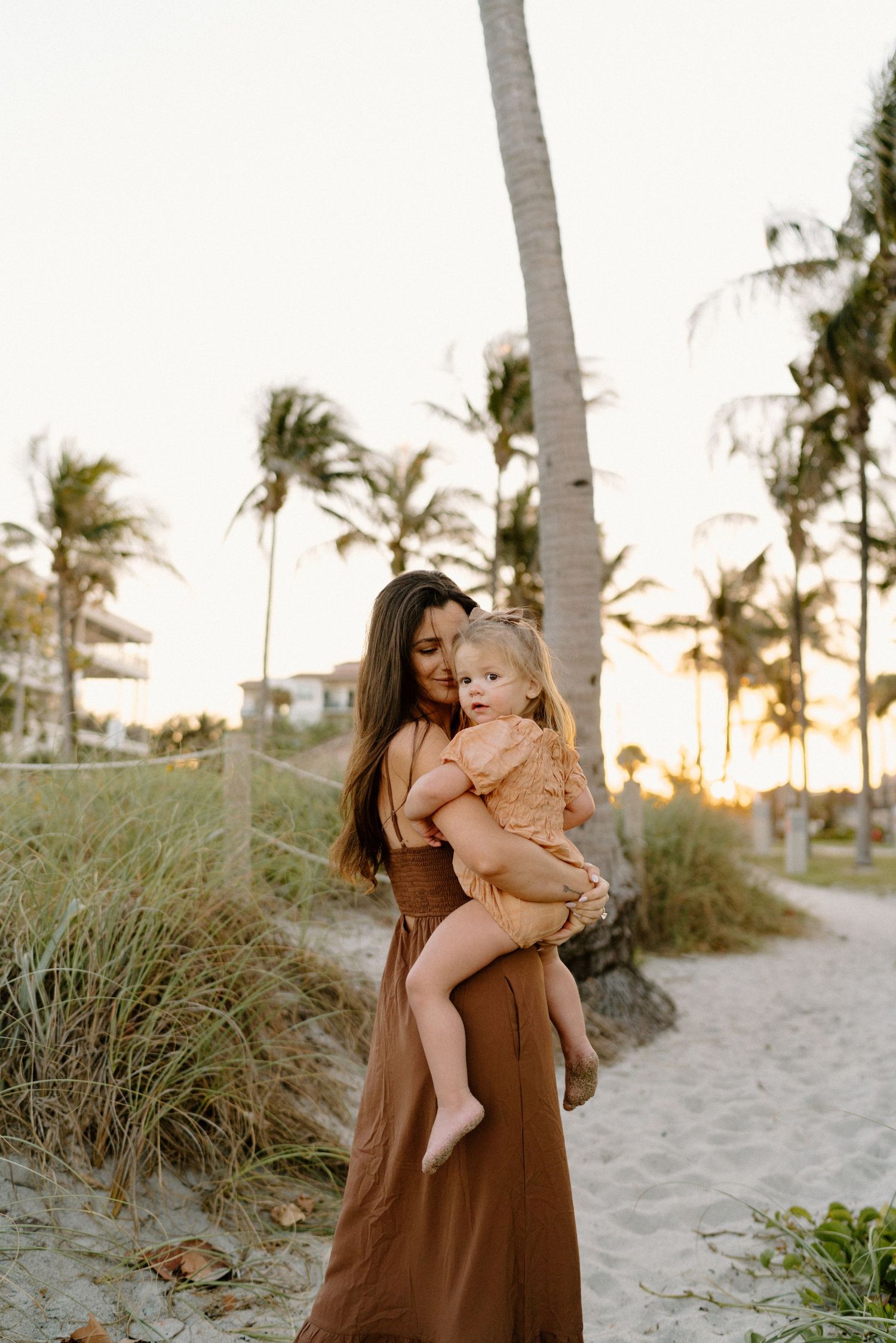 A tender moment captured at sunset on a tropical beach with palm trees in the background.