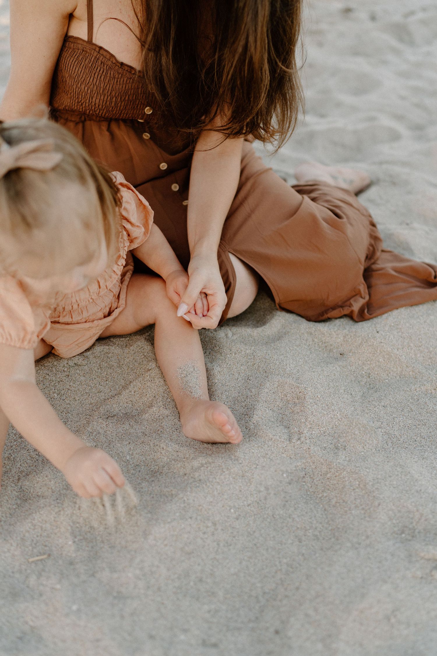 Close-up shot of people sitting on sandy beach wearing earth-toned dresses.
