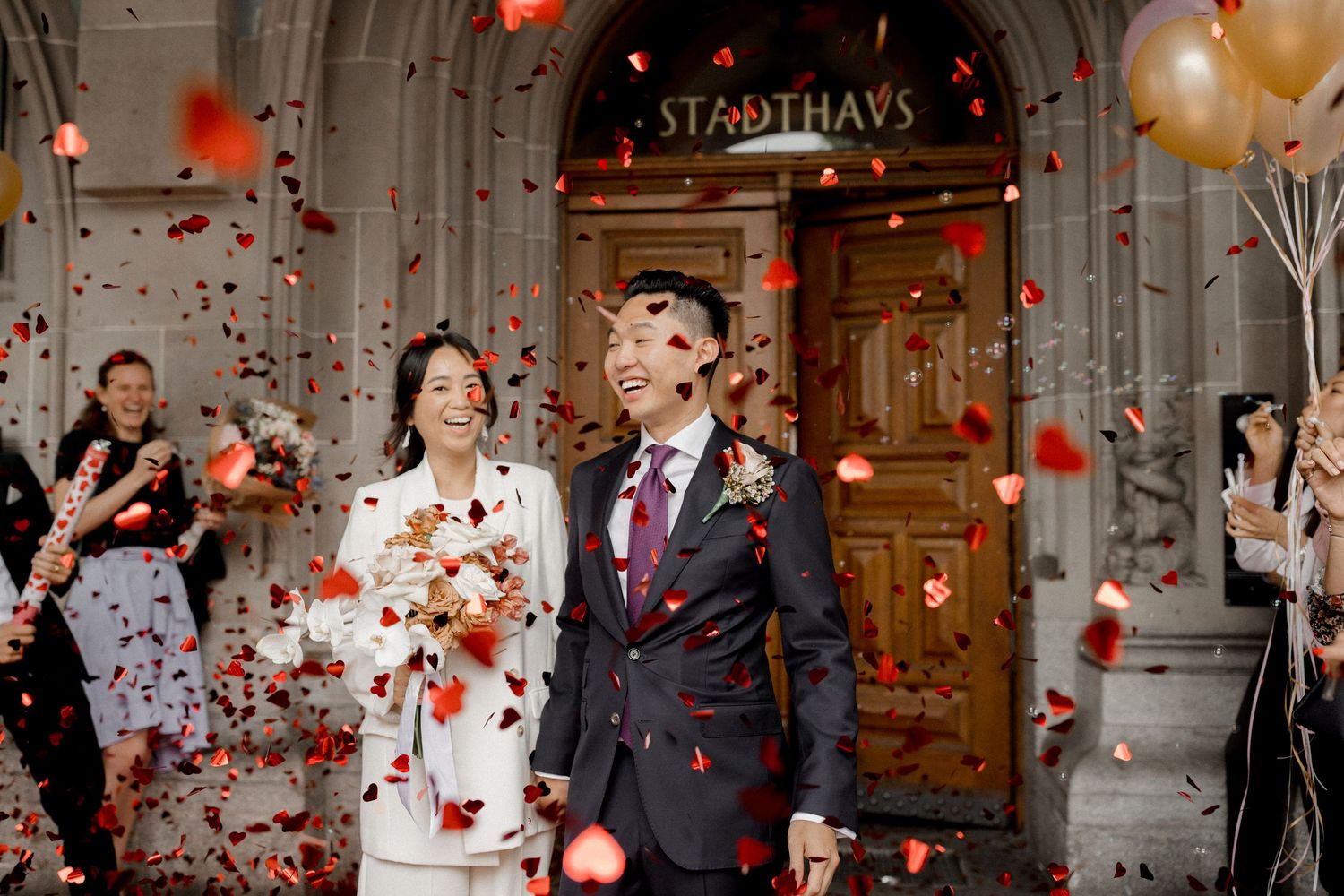 Wedding celebration with red confetti and balloons in an elegant indoor venue. Stadthaus Zürich.