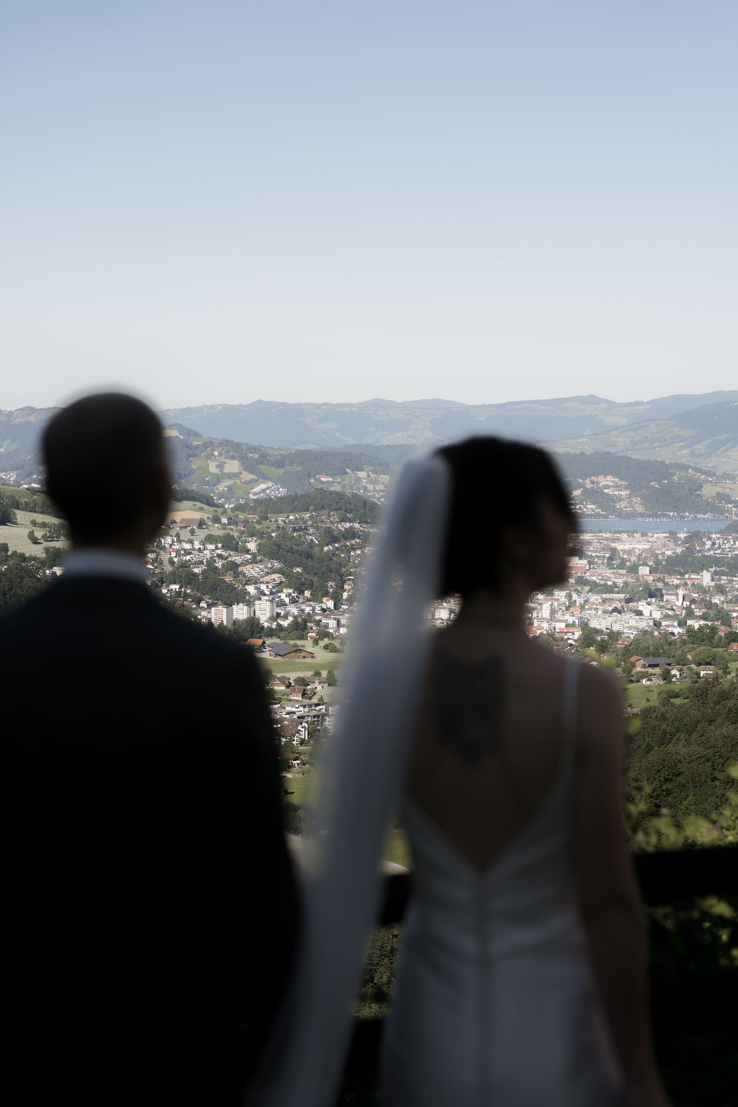 Bride and groom stand with backs turned, overlooking a scenic mountain town valley on their wedding day.