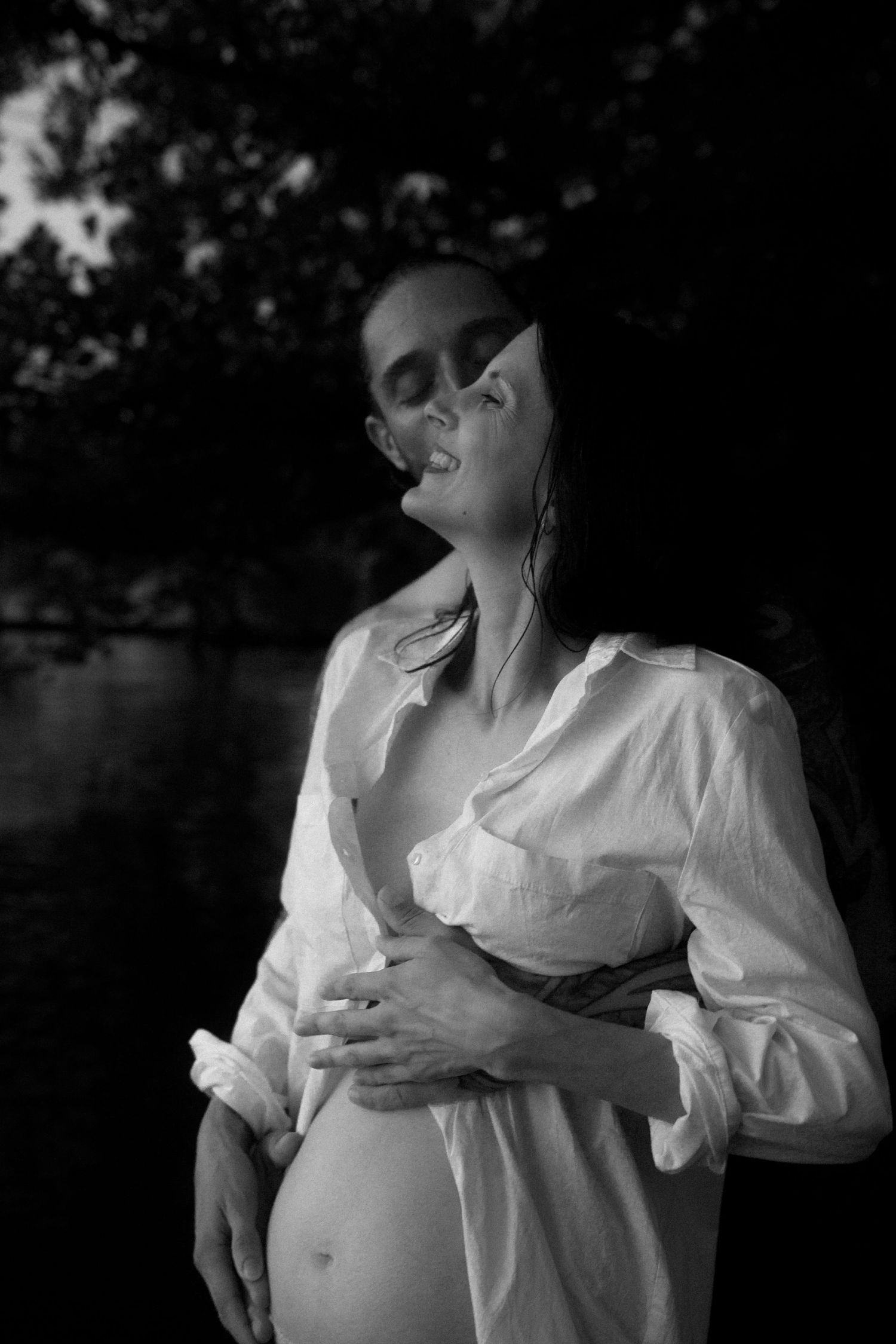Artistic black and white maternity photo with woman in white shirt outdoors.