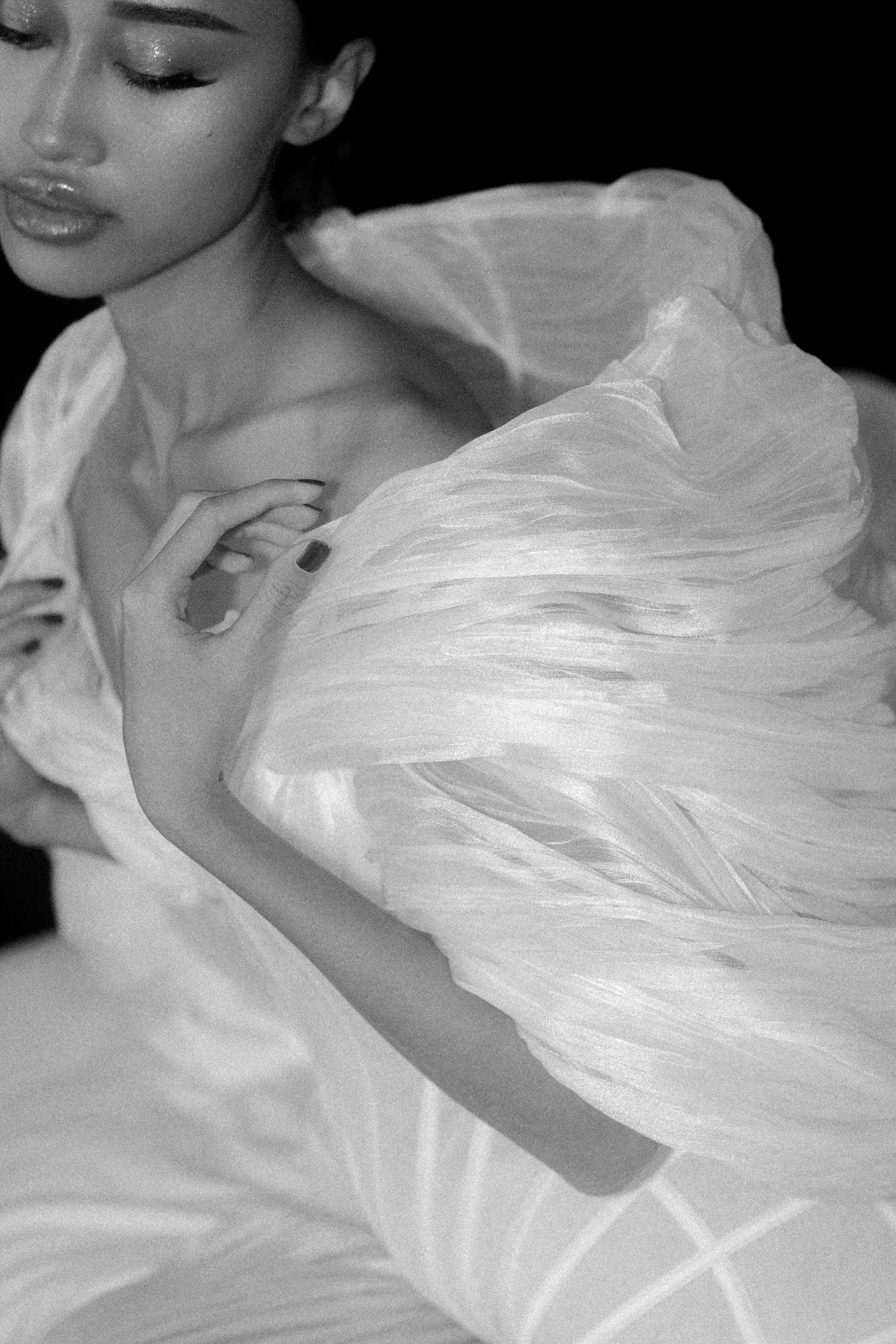 Black and white photo of a woman in a flowing white feathered gown, eyes closed, hands crossed over chest.