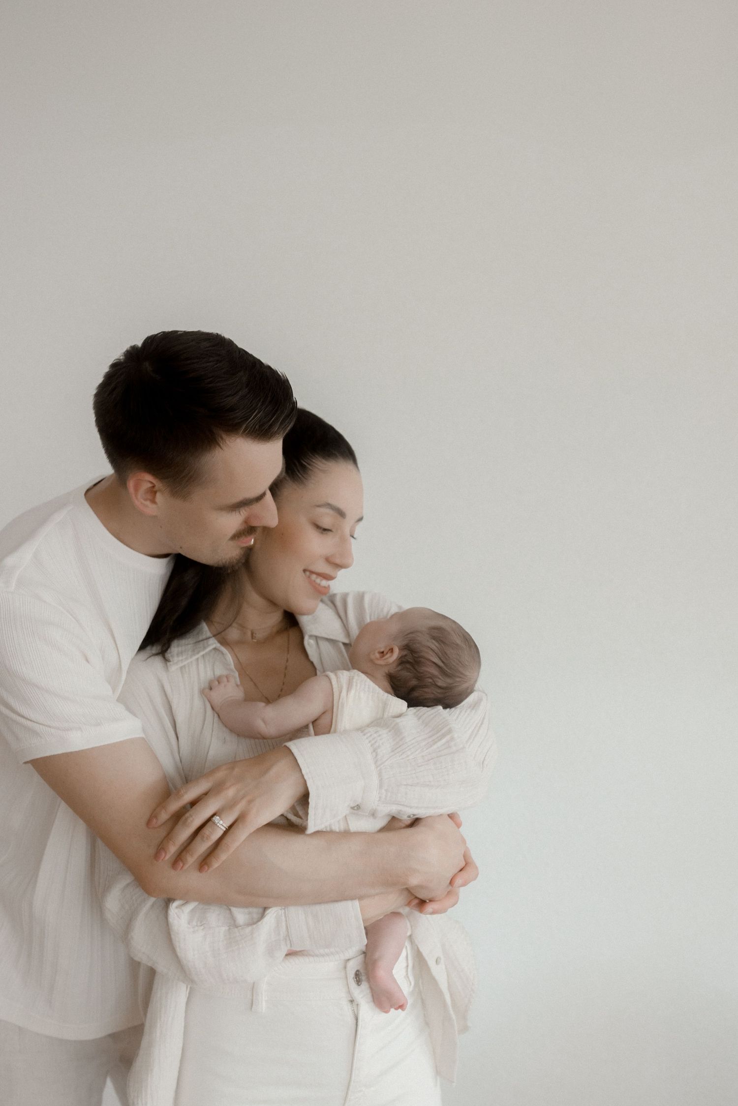 Tender moments between parent and newborn baby captured in soft white tones.