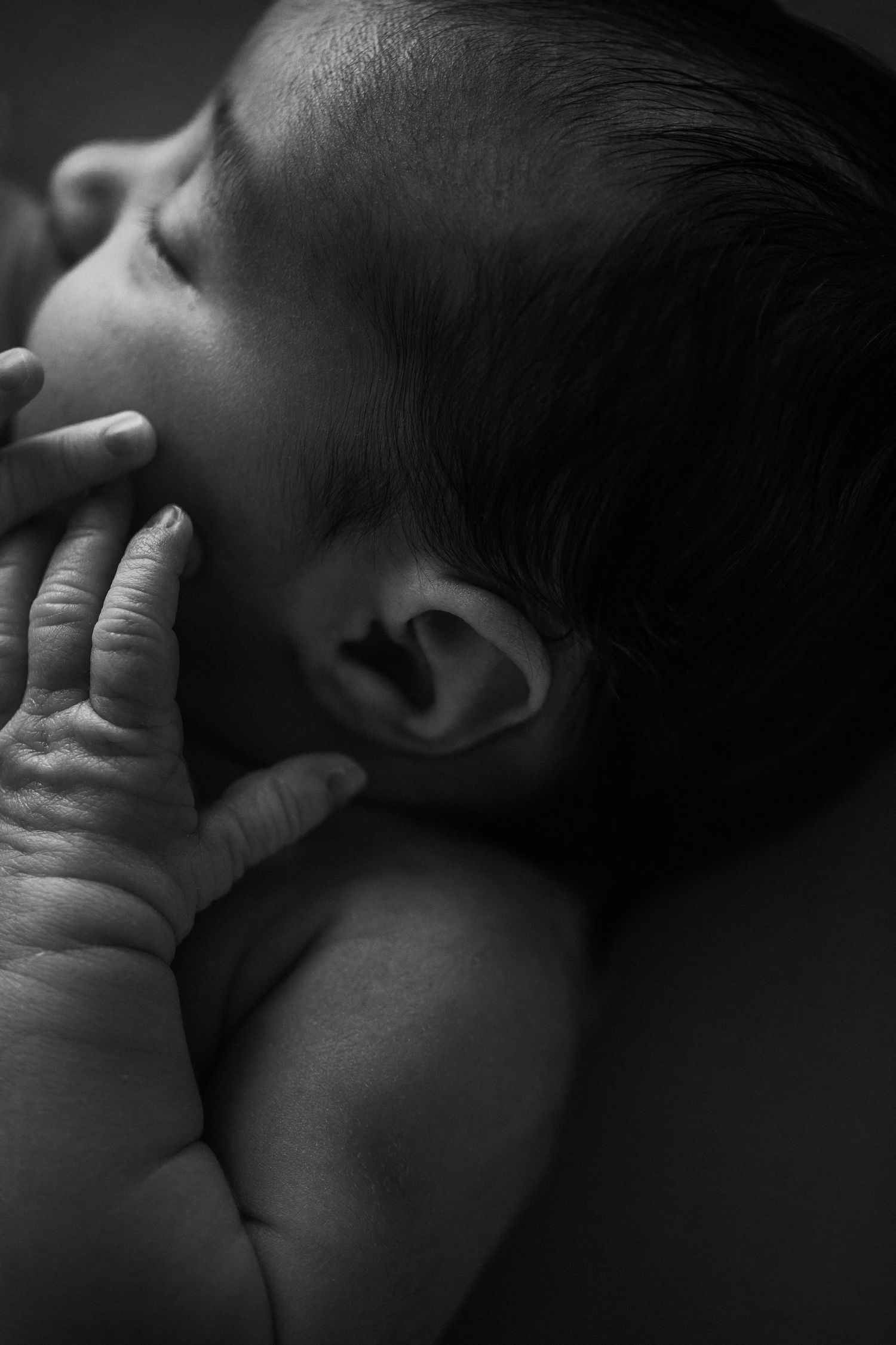 Black and white close-up of a baby's profile showing tiny fingers near their face in a tender, peaceful moment.