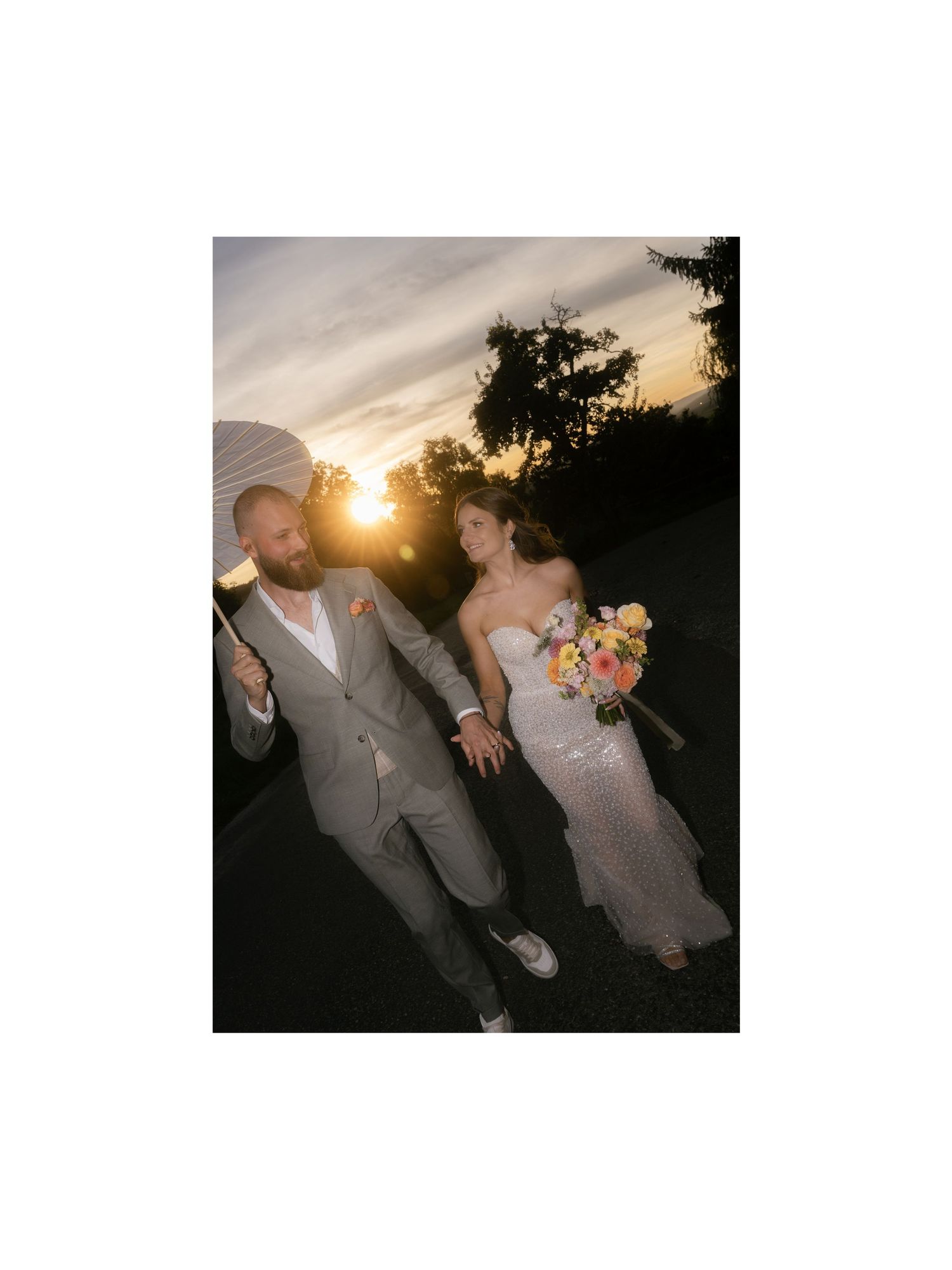 A couple in wedding attire dances together at sunset, creating a romantic silhouette against the golden sky.
