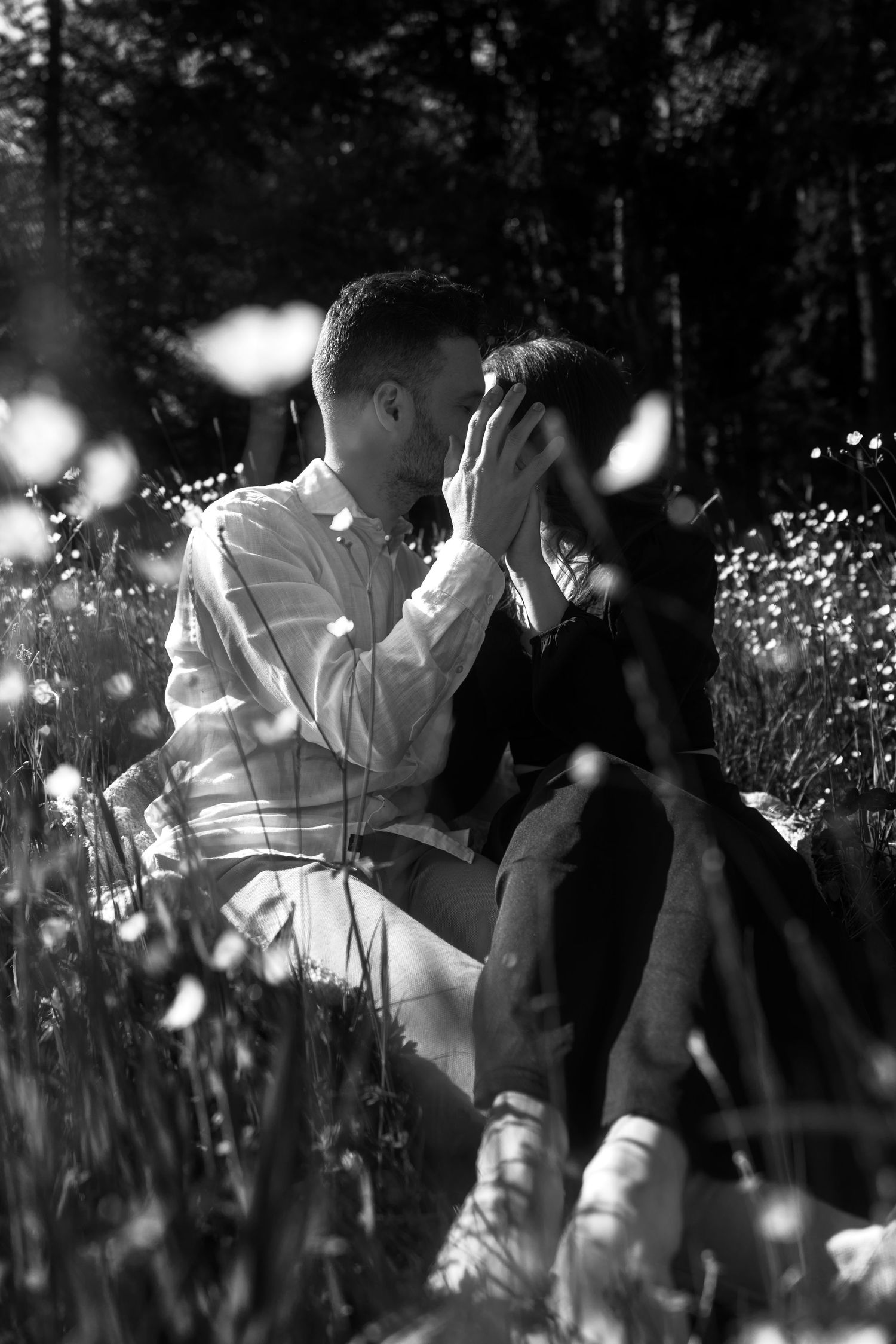 A romantic black and white photograph of a couple sharing an intimate moment among wildflowers in a meadow.