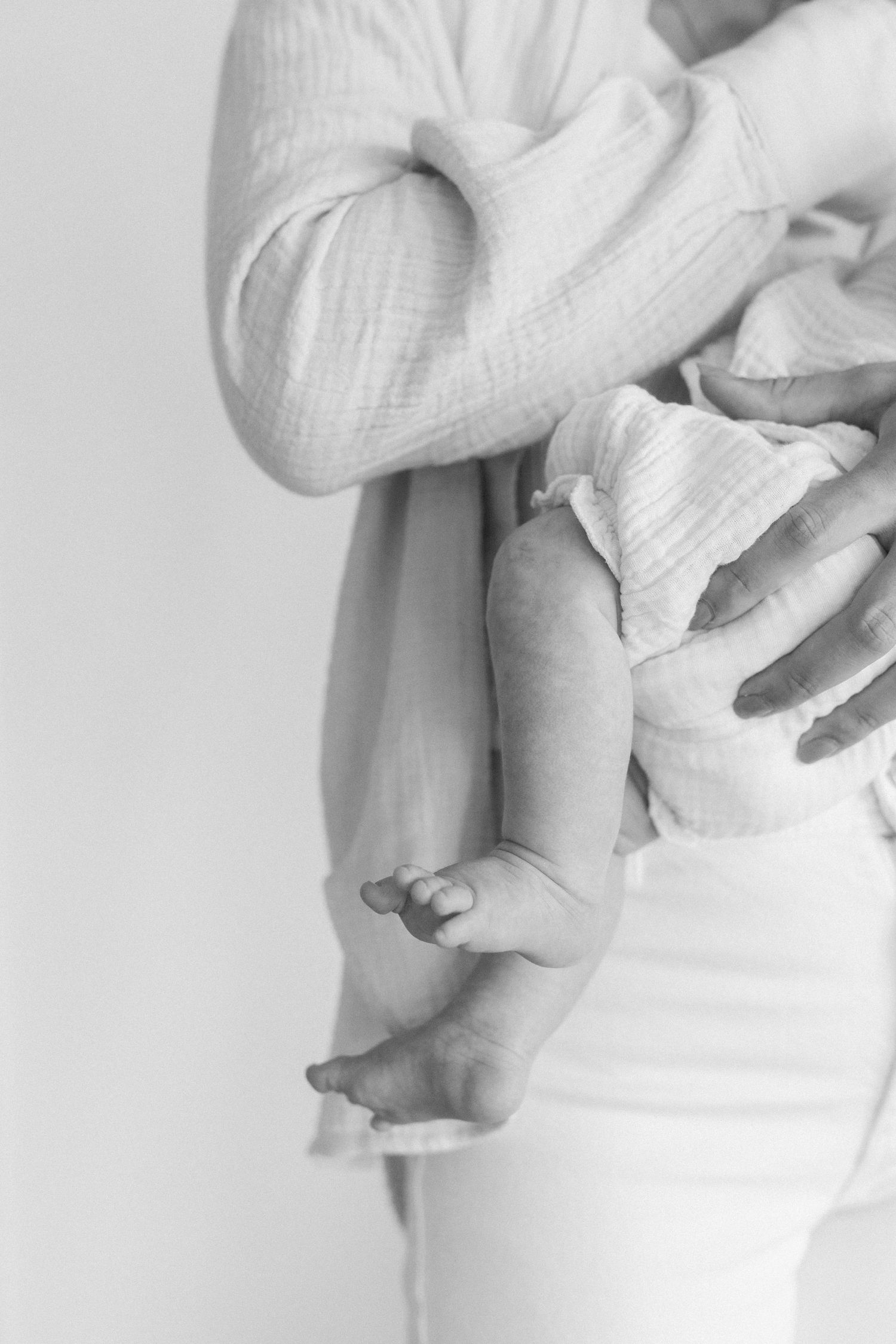 Close-up details of hands holding newborn baby wrapped in white fabric.
