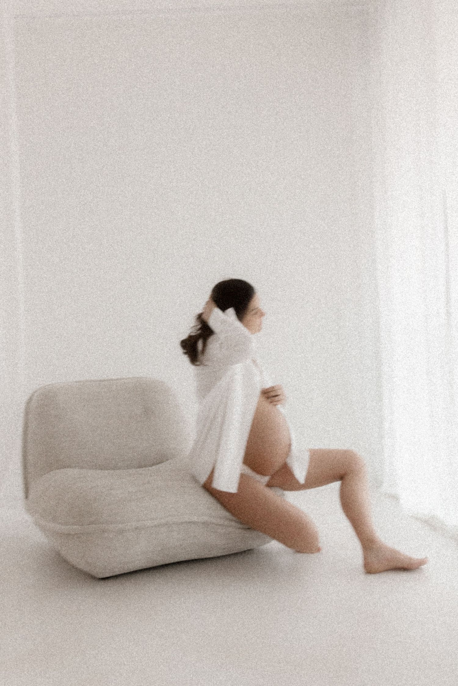 Soft, minimalist portrait of person resting on beige couch in white room.