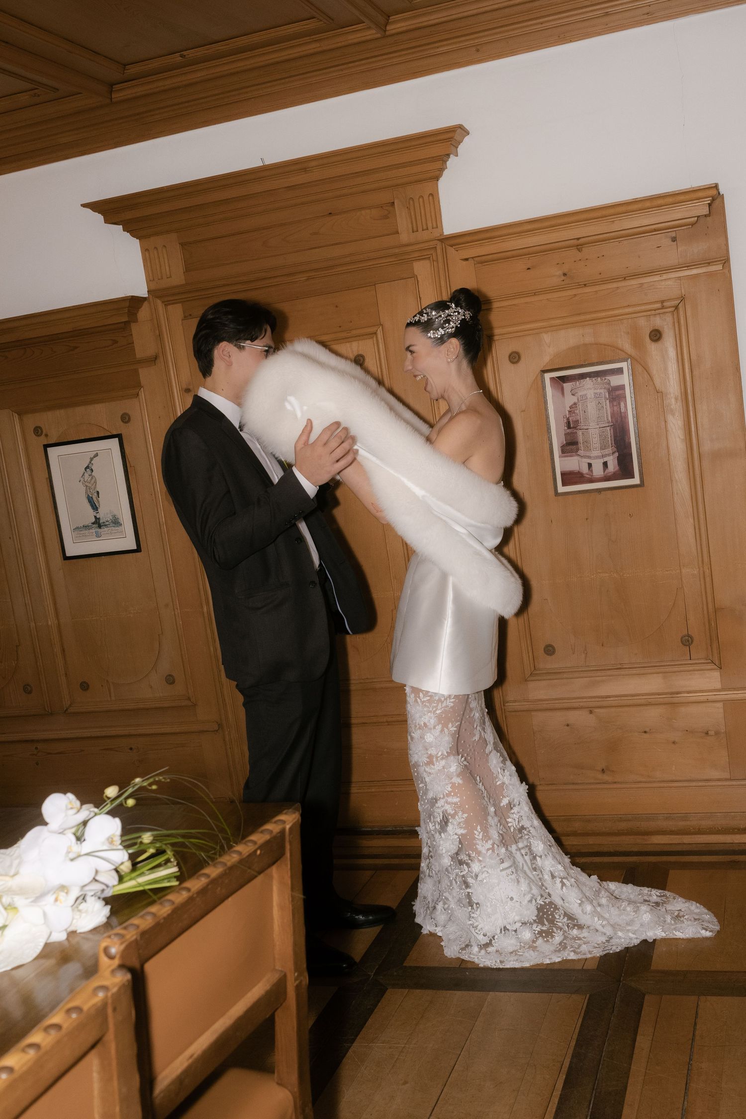 Bride and groom share a romantic moment in a wooden chapel, bride wearing lace wedding gown with fur wrap.