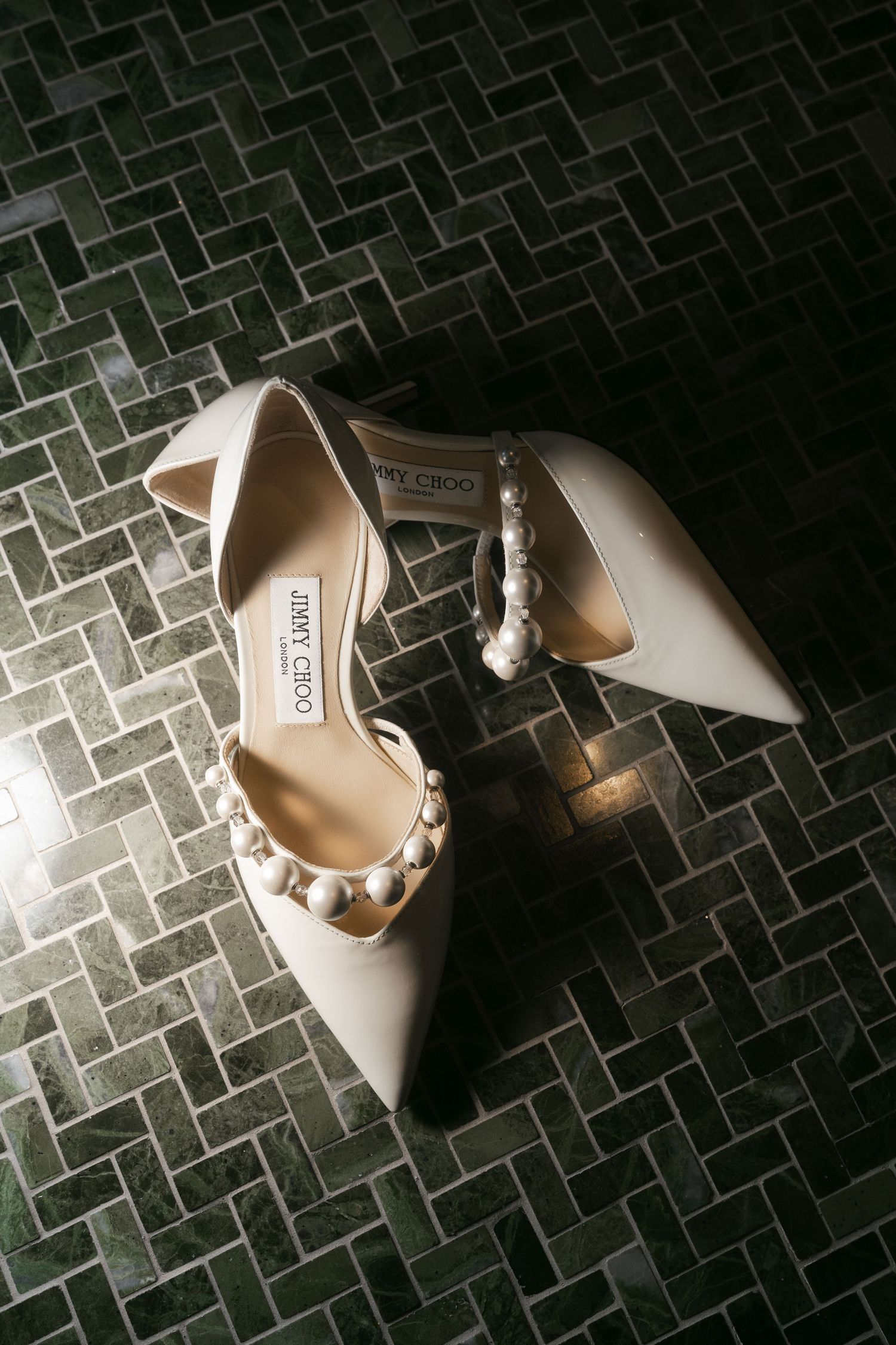 Jimmy Choo ivory pearl-embellished pointed-toe heels displayed on dark herringbone tile floor.