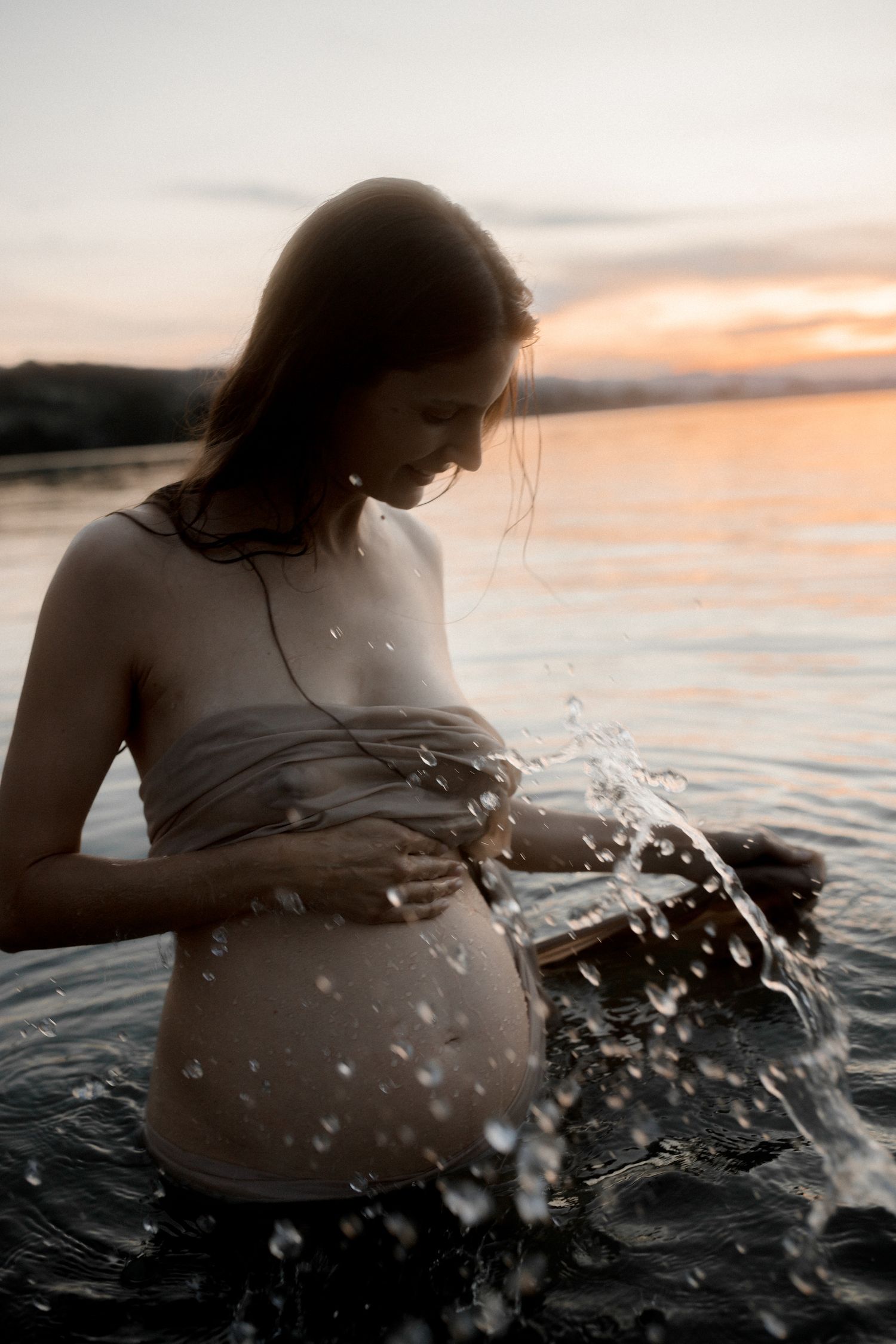 Dramatic sunset maternity photos in water with splashing effects.
