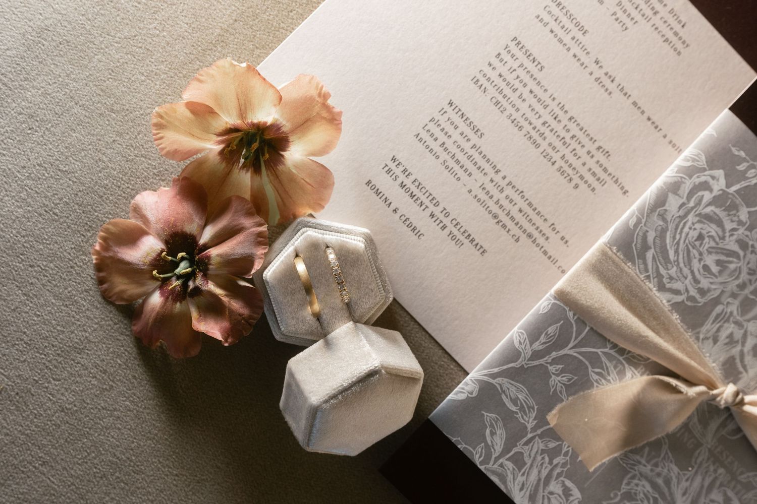 Elegant wedding invitation with floral decor, ring box, and satin ribbon on a neutral background.