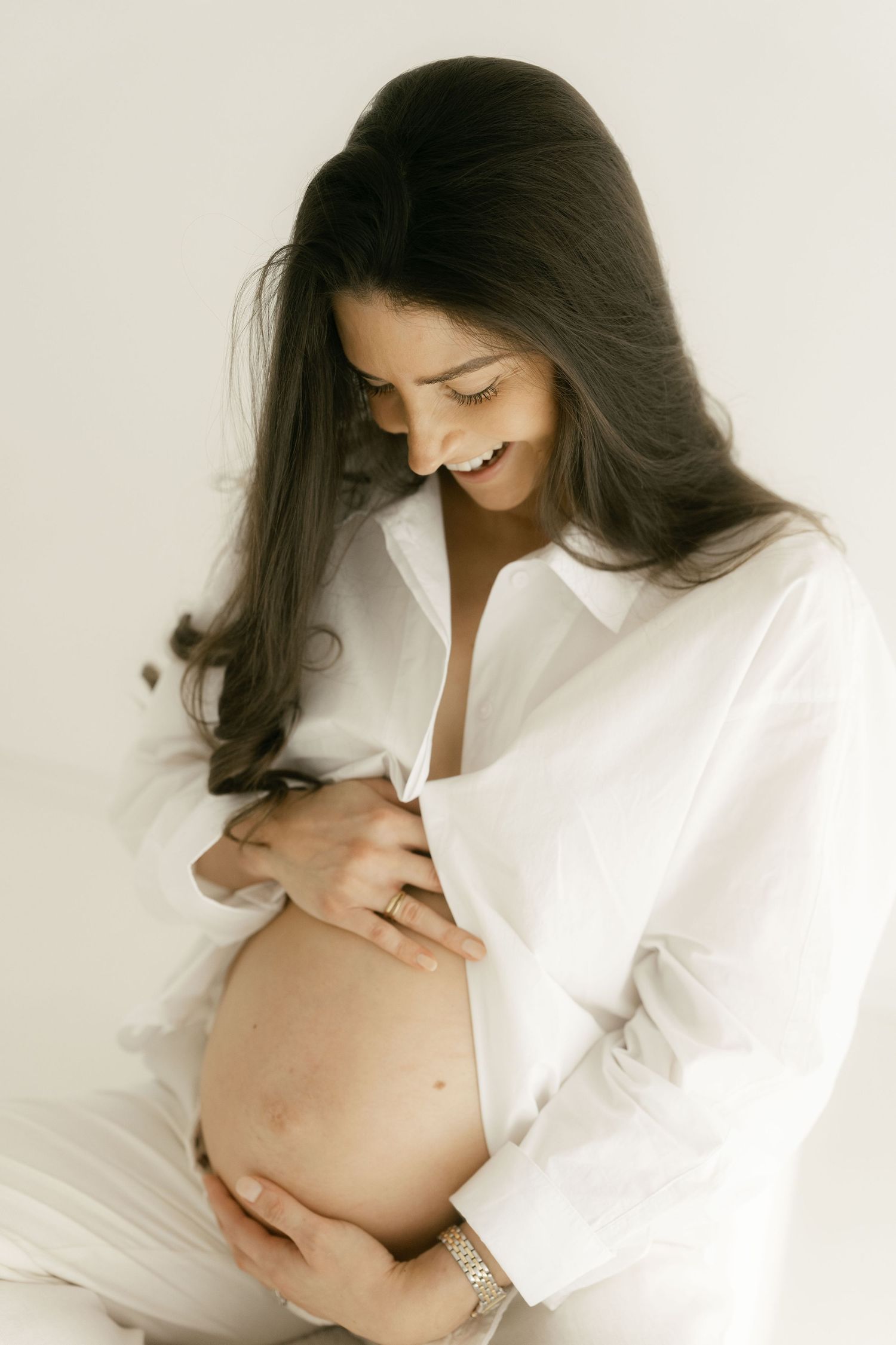 Elegant maternity photoshoot featuring a white button-down shirt and natural lighting.