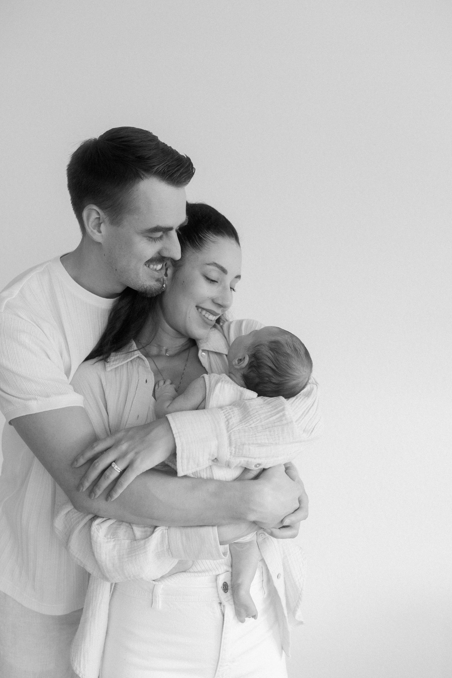 Intimate black and white portrait of parents embracing their newborn baby.