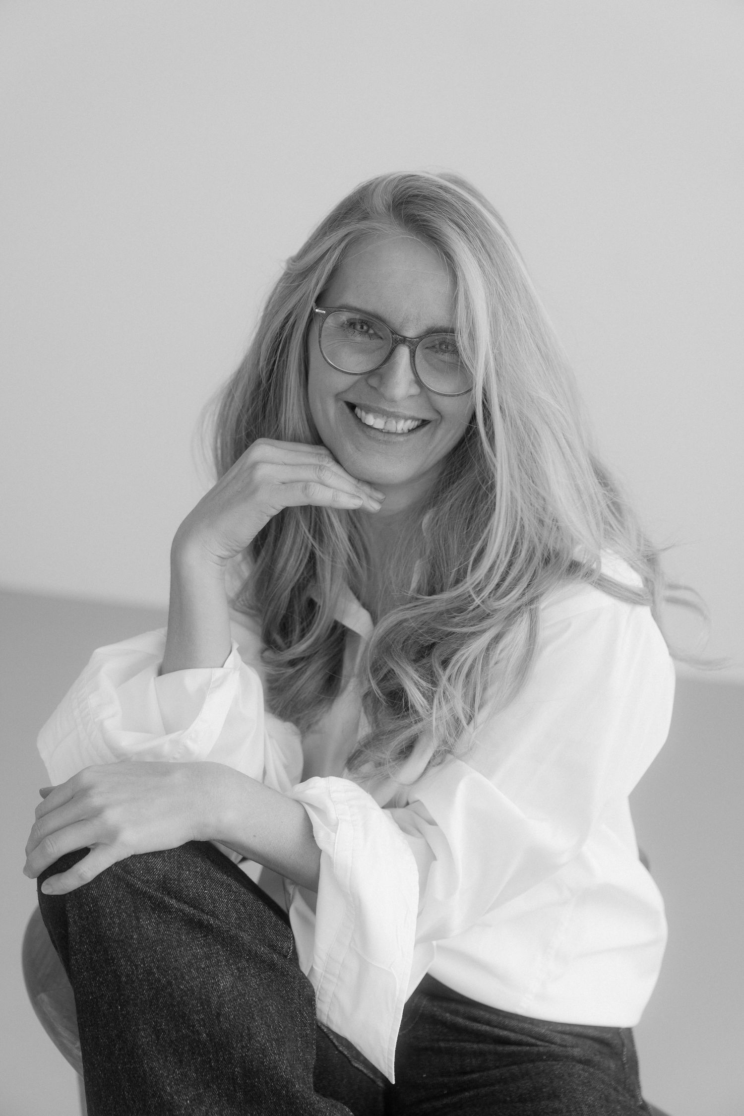 Black and white photo series of someone with blonde hair wearing glasses and a white top posing against a light background.