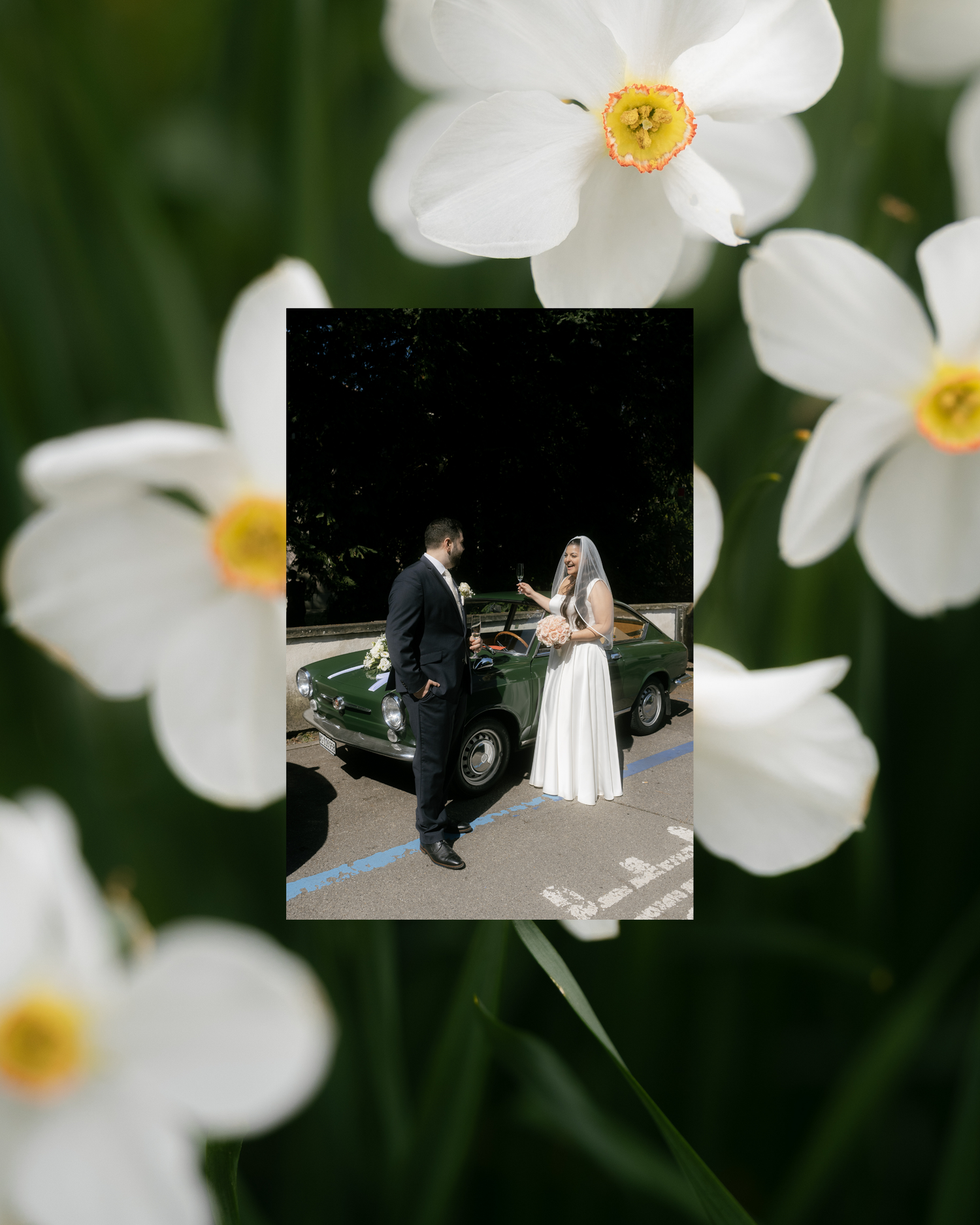 Bride and groom standing by a vintage green car, framed by white daffodil flowers in soft focus.