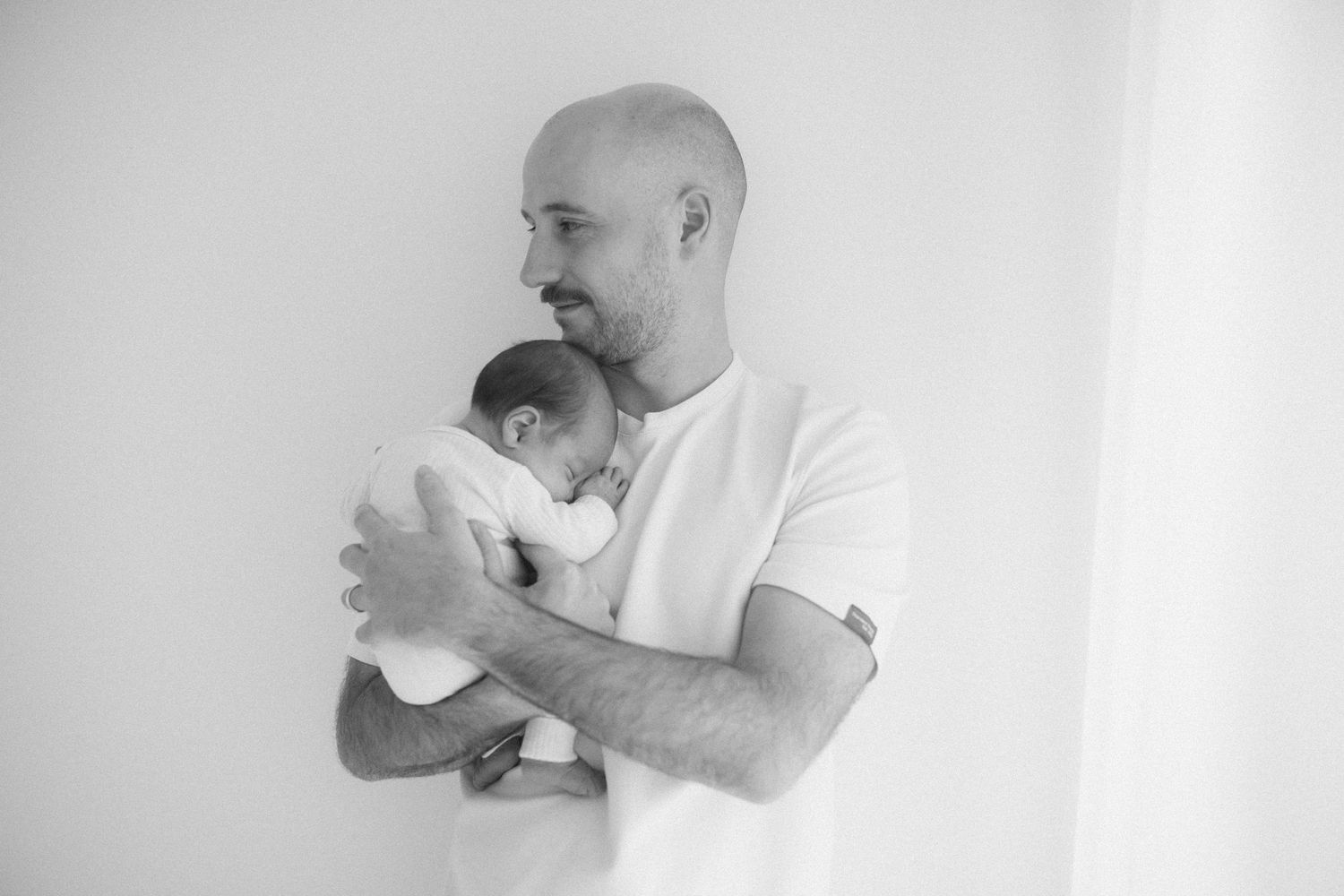 Black and white portrait of parent holding newborn baby against white wall.