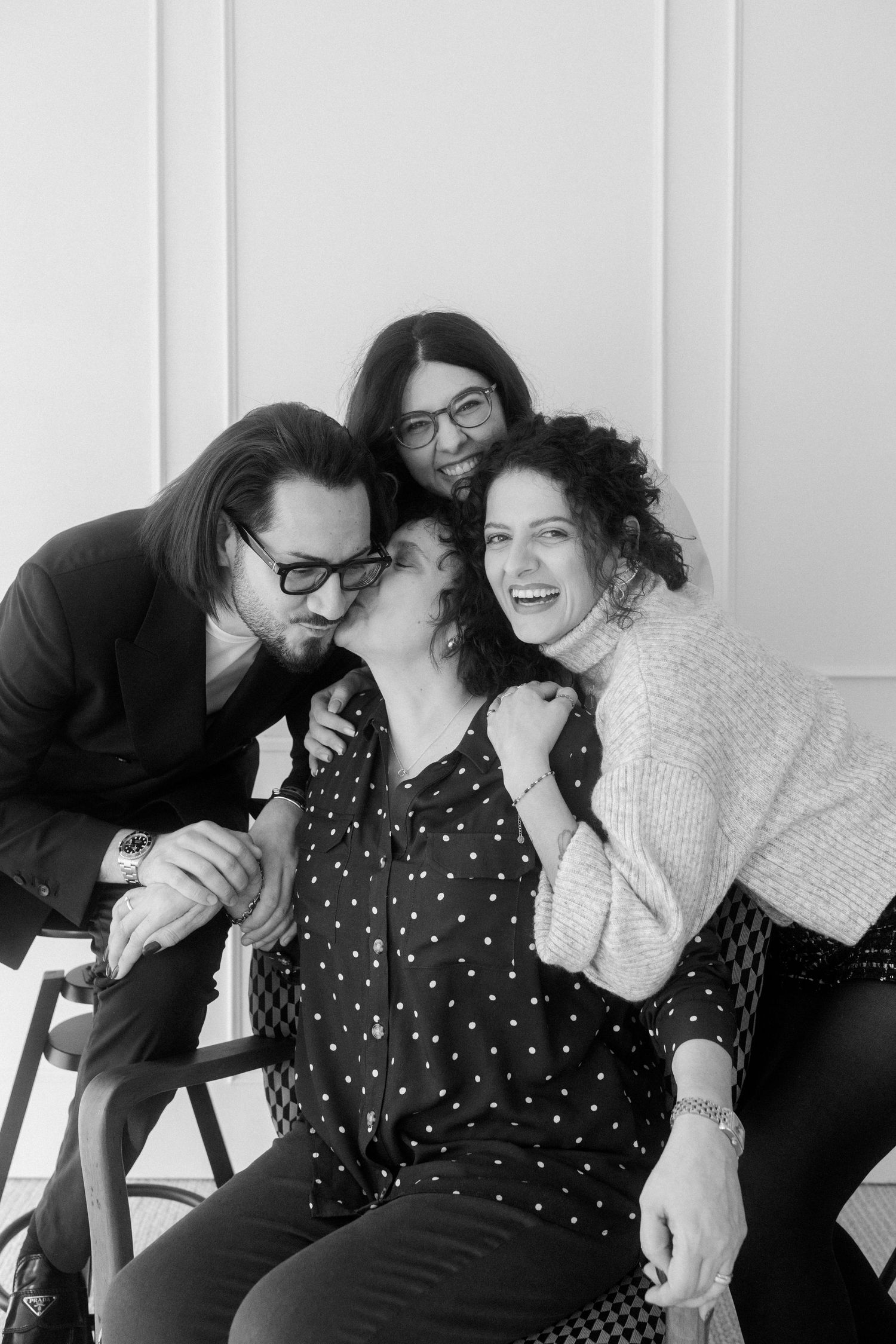 Black and white candid photos showing joyful laughter and embraces against a white wall.