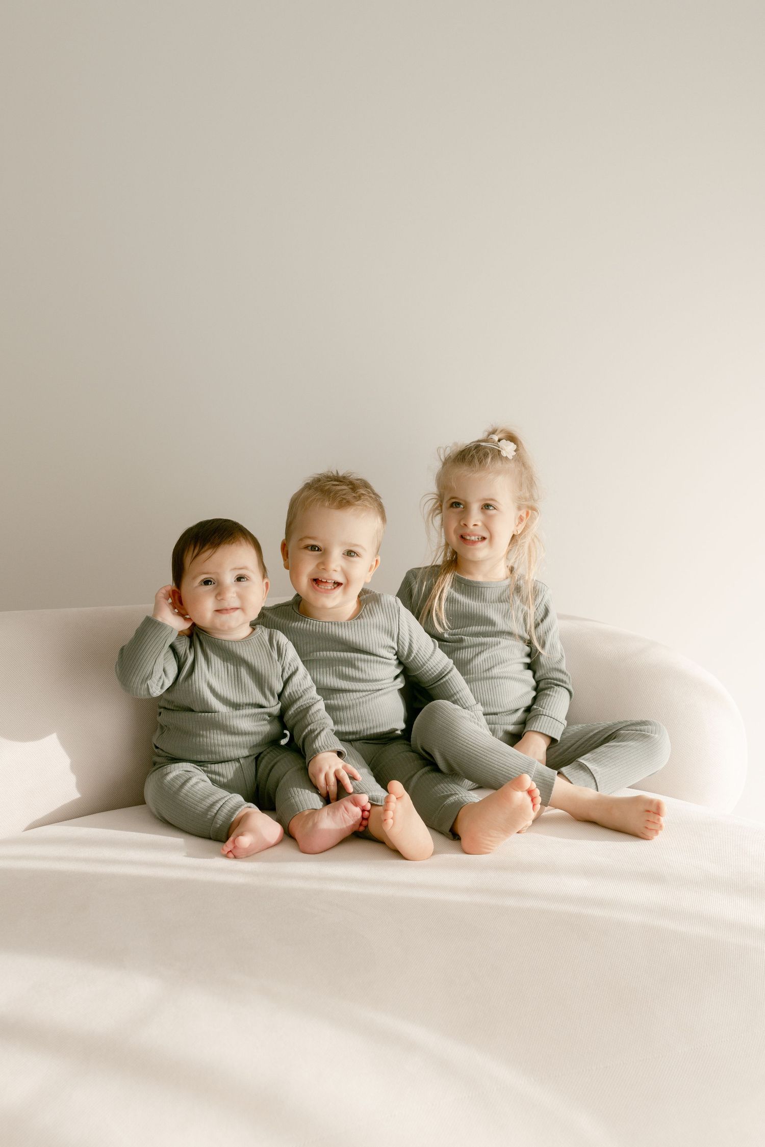 Three toddlers in matching grey outfits sitting together against white background.