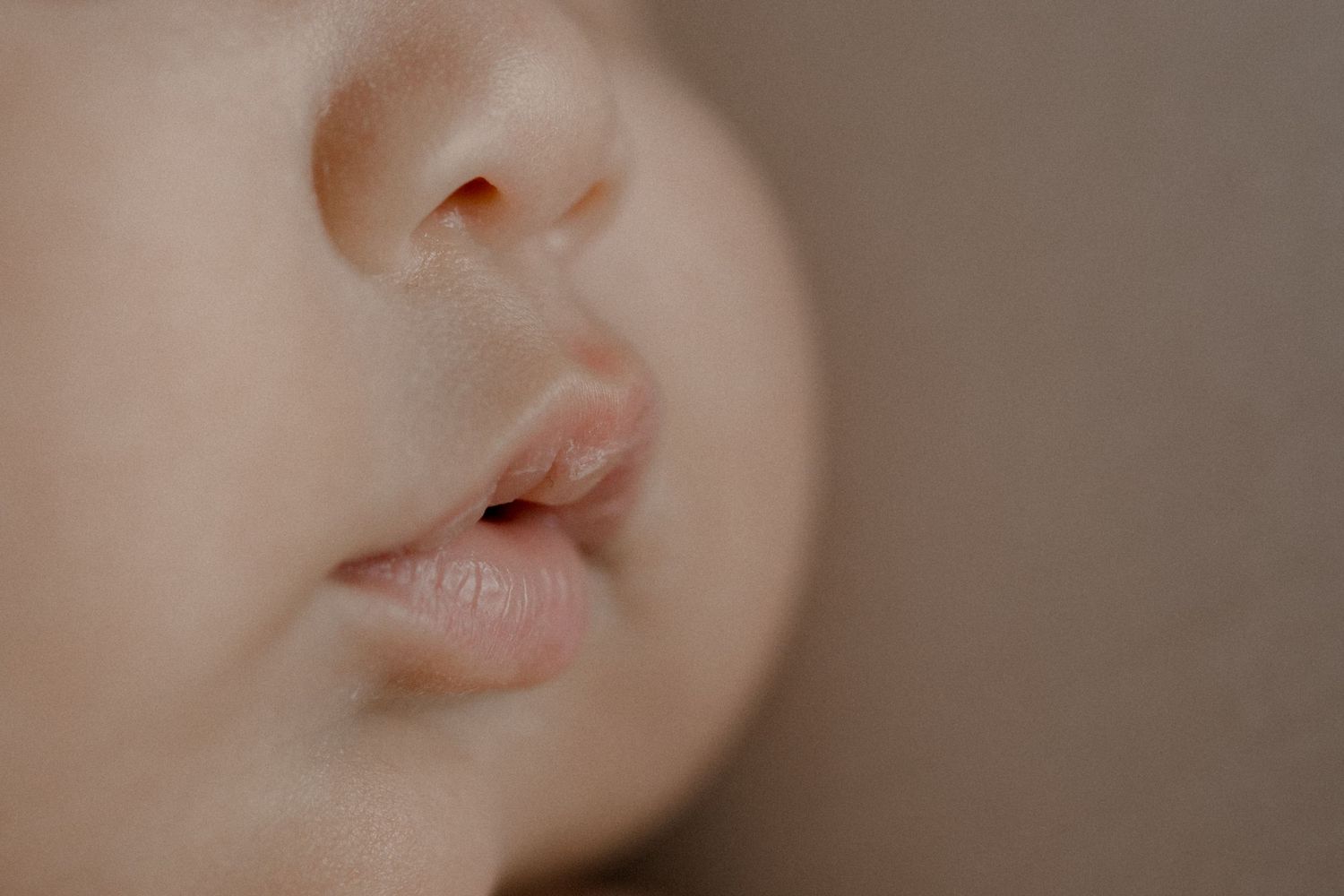 Extreme close-up of soft pink lips and nose in gentle lighting.