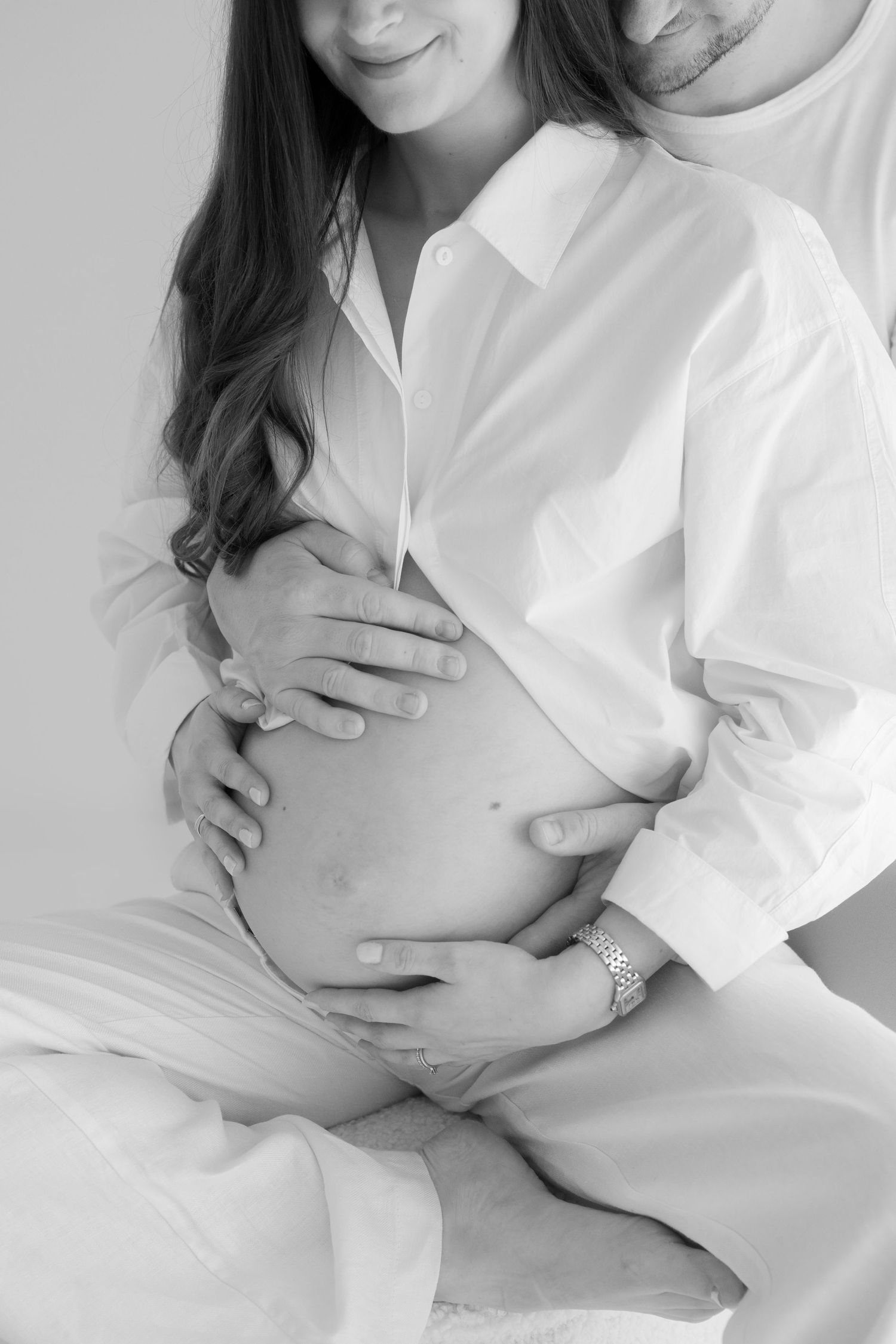 Intimate maternity photo series in white showing close embrace and tender moments against light background.