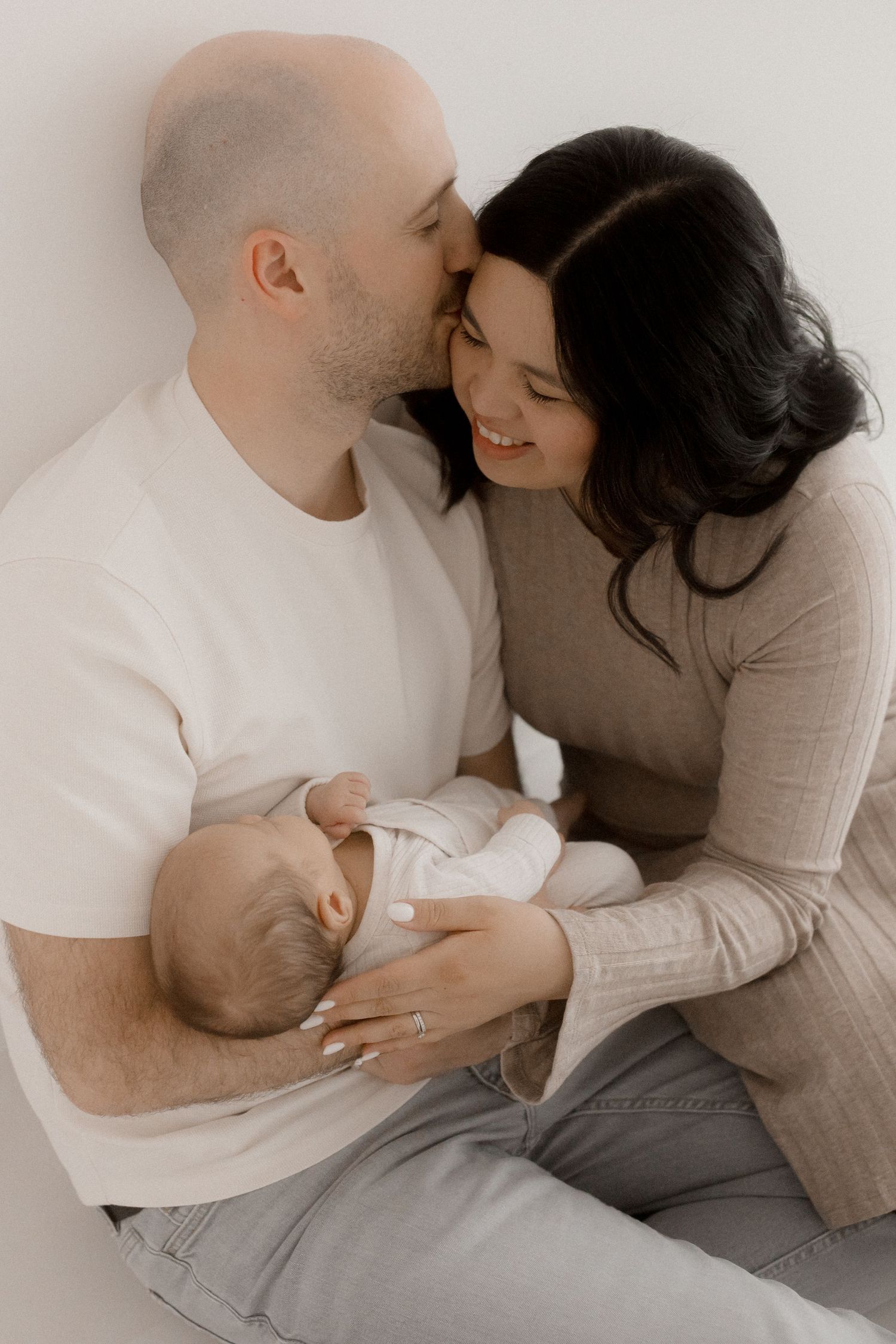 Tender family moment with newborn baby in minimalist neutral setting.