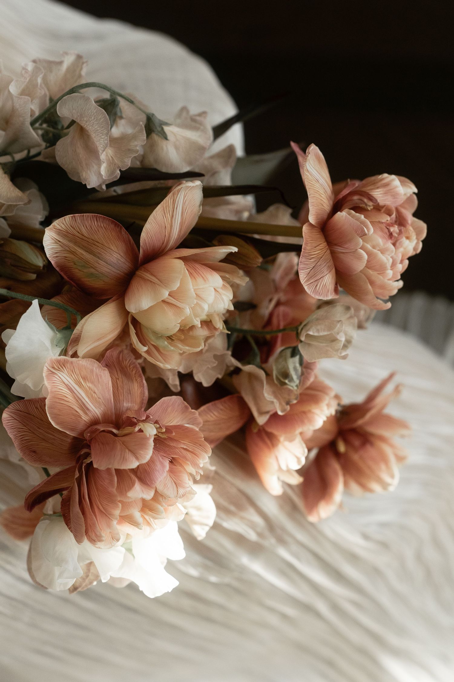 Elegant bouquet of blush pink and white tulips and peonies arranged on soft white fabric in natural light.