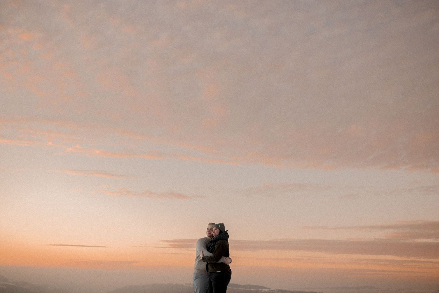 A silhouetted couple shares a romantic moment against a pink and orange sunset sky.