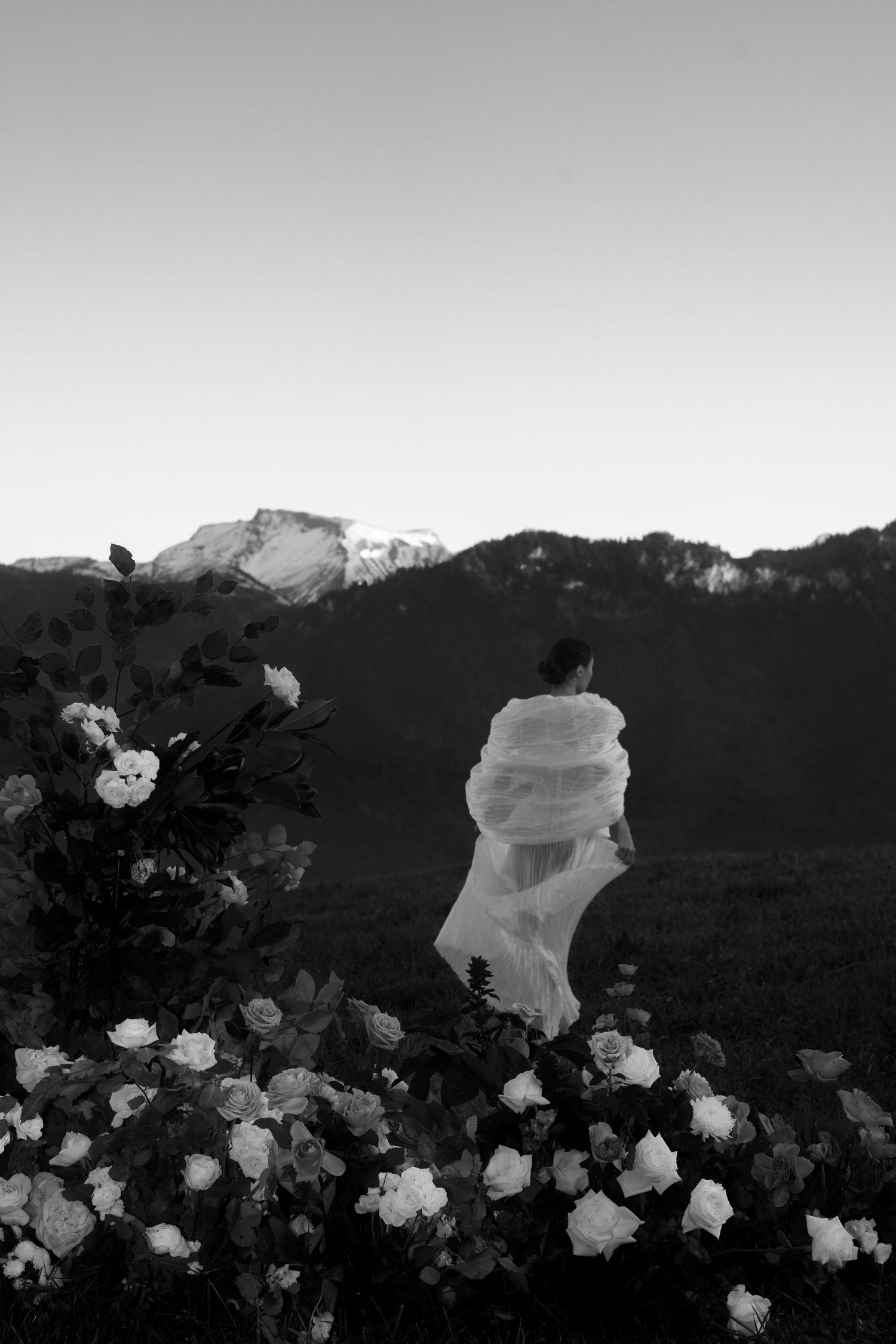 Ethereal silhouette in flowing white dress against mountain landscape with roses in foreground at Villa Honegg Bürgenstock.