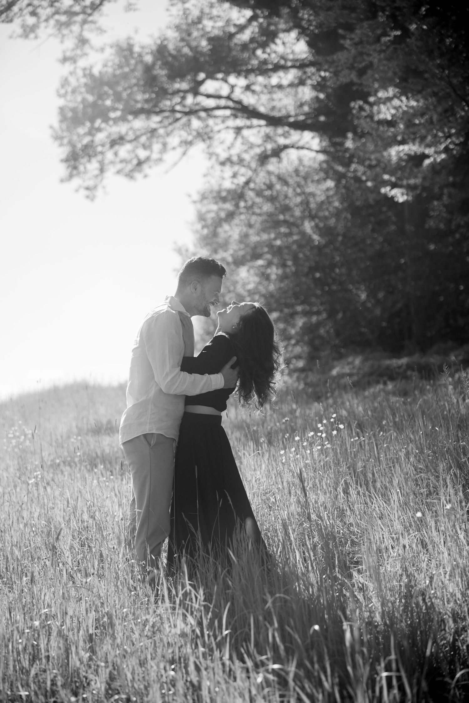Romantic couple embracing in tall grass field at sunset in black and white photography.