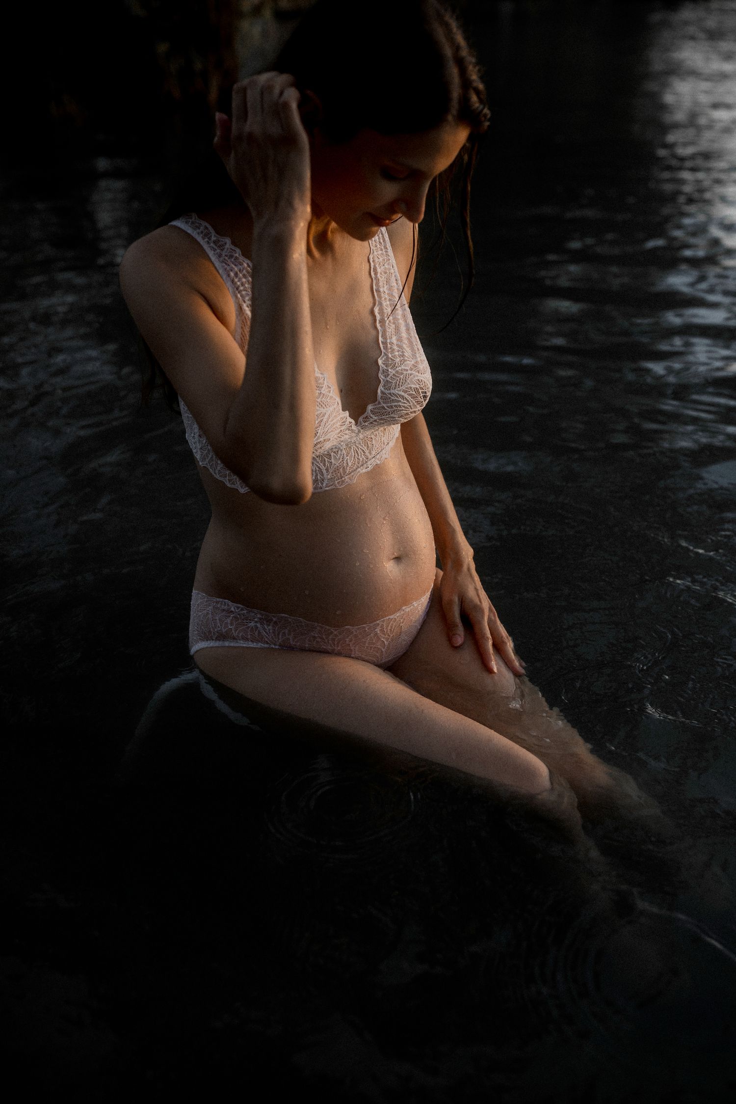 Artistic maternity photo with subject sitting in water during golden hour.