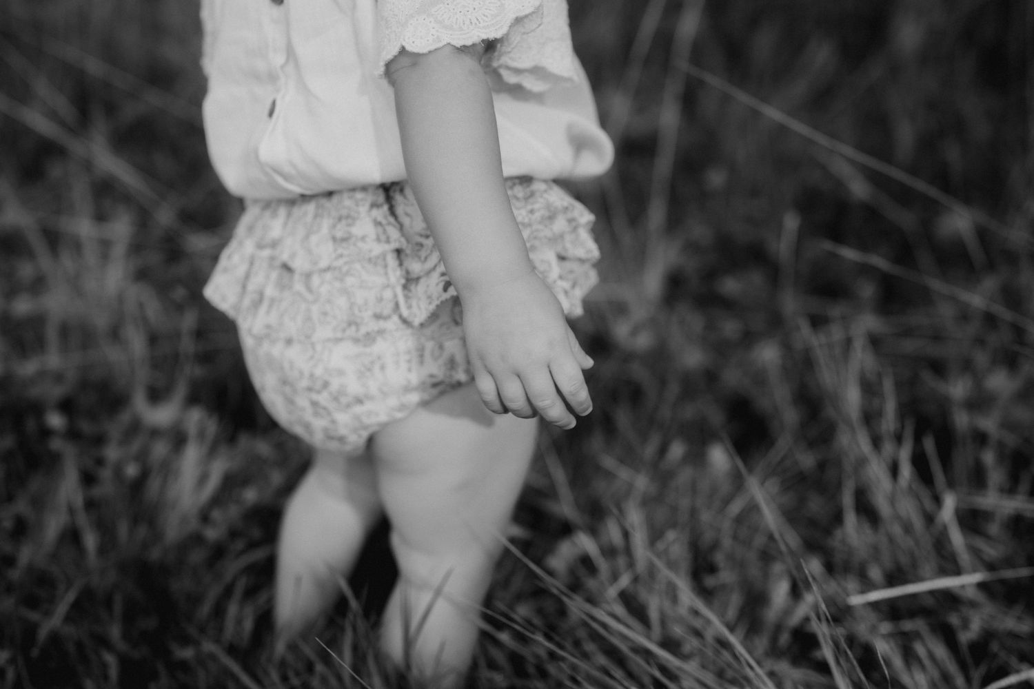 Close-up black and white shots of small children's legs and feet in a field.