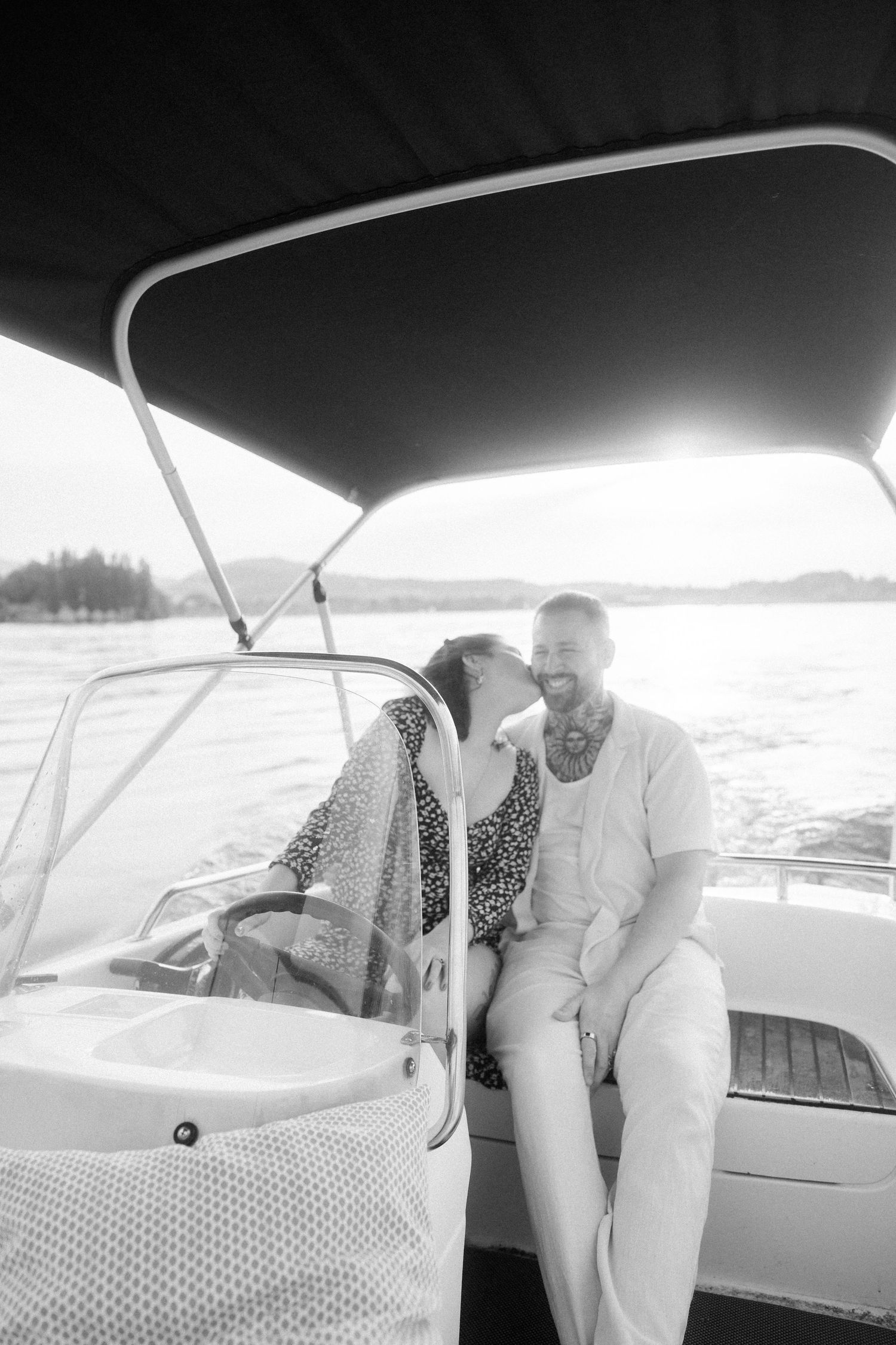 A couple shares a romantic moment together on a boat under a canopy on a sunny day at the lake.