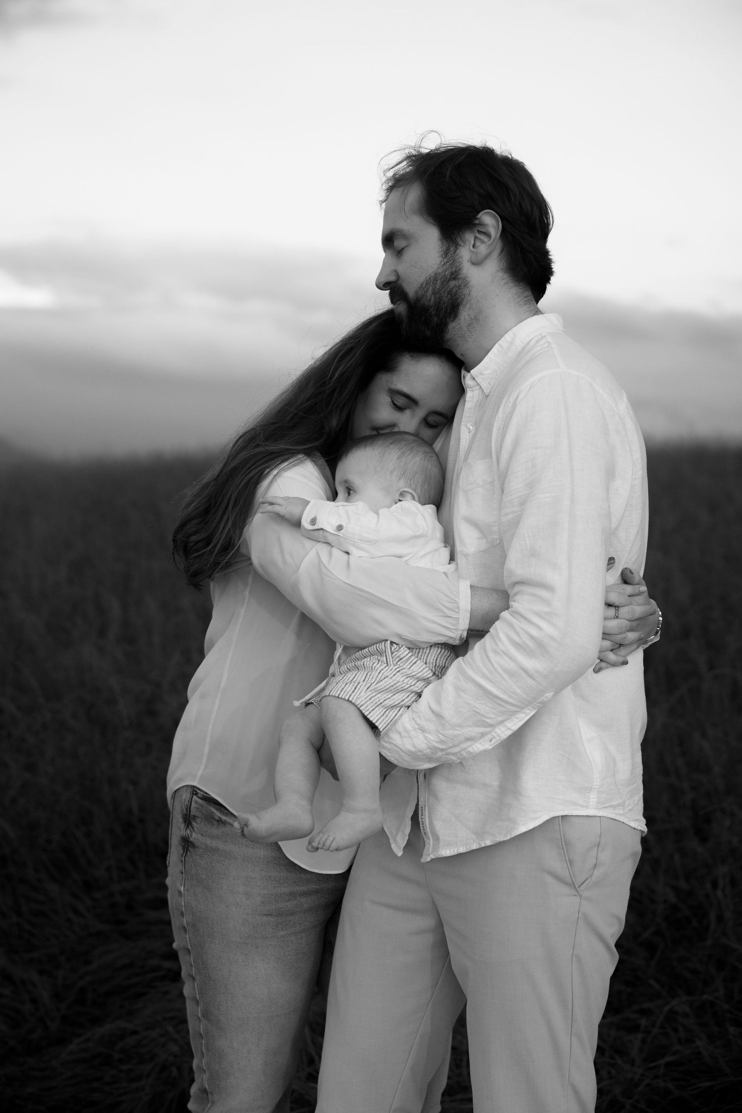 Family embracing in white clothing against dramatic landscape at dusk.