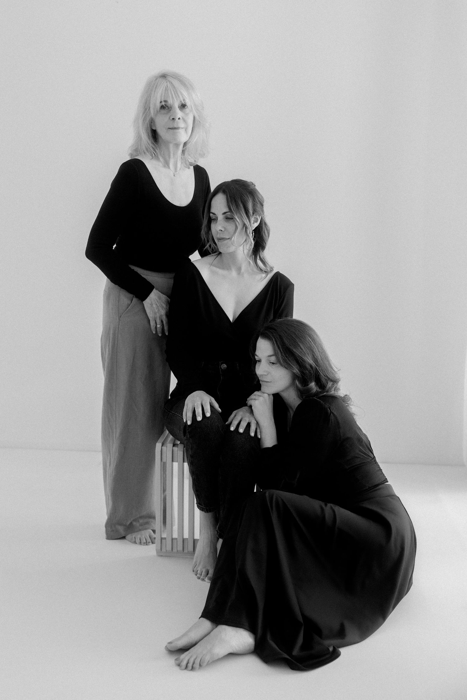 Black and white artistic photo series showing two figures in dark clothing posing together on a light background.