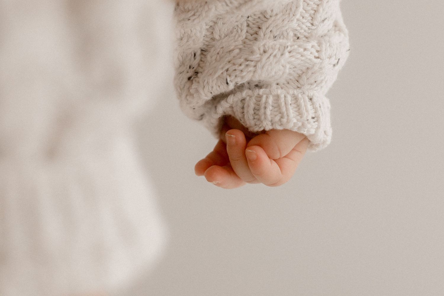 Close-up shot of a baby's tiny hand grasping against a soft white textured background.