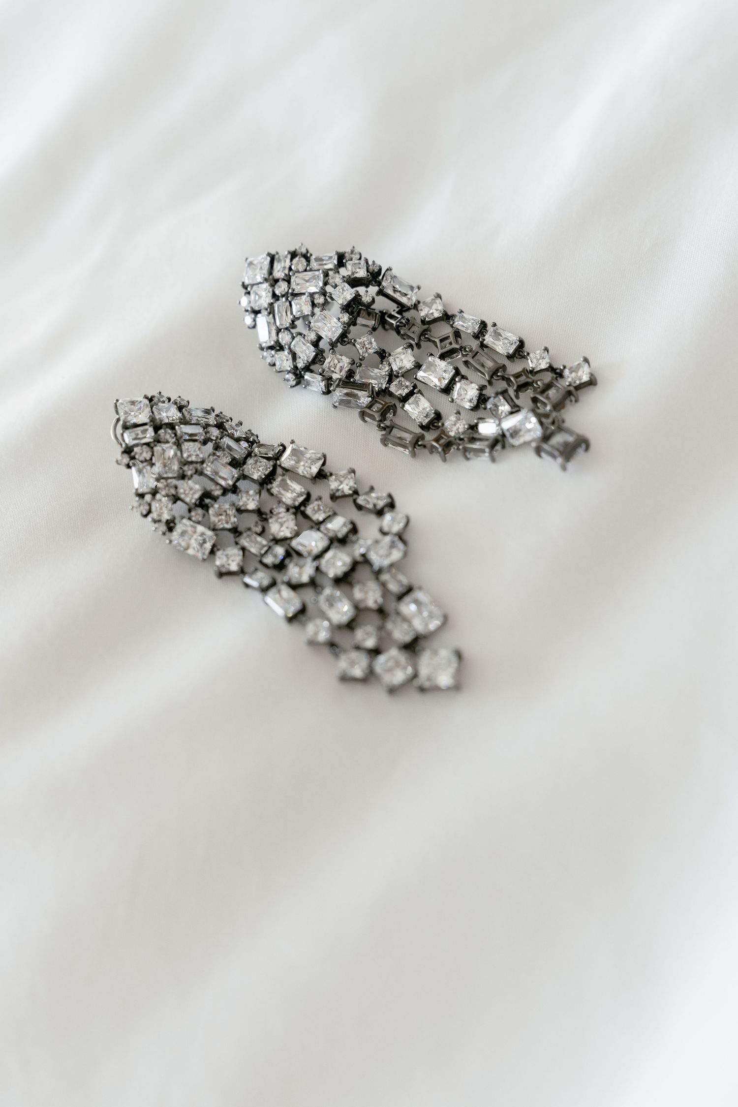 Elegant silver rhinestone drop earrings with cascading crystal embellishments on white fabric background.