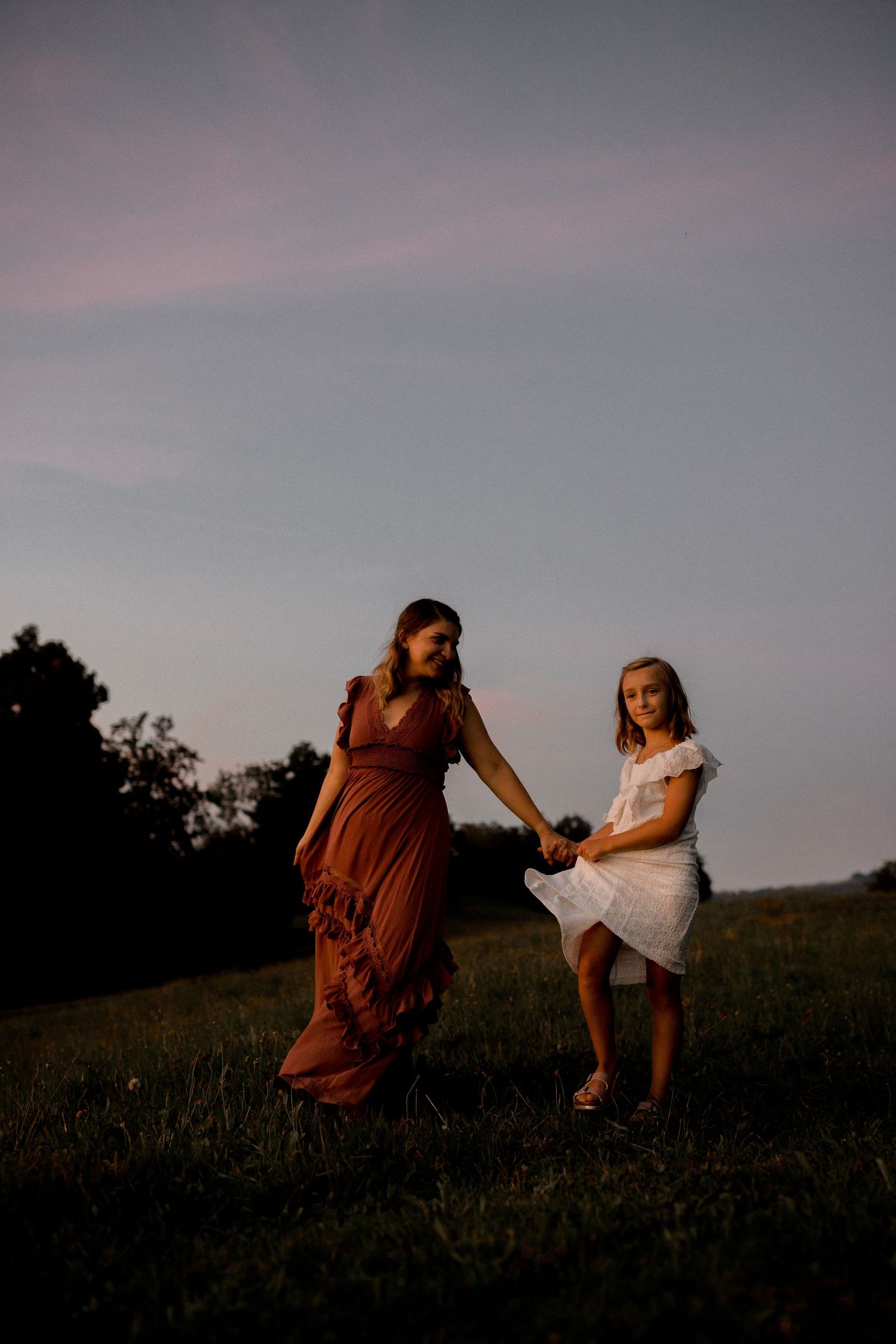 Silhouettes of people in dresses sitting on a grassy hill during sunset.