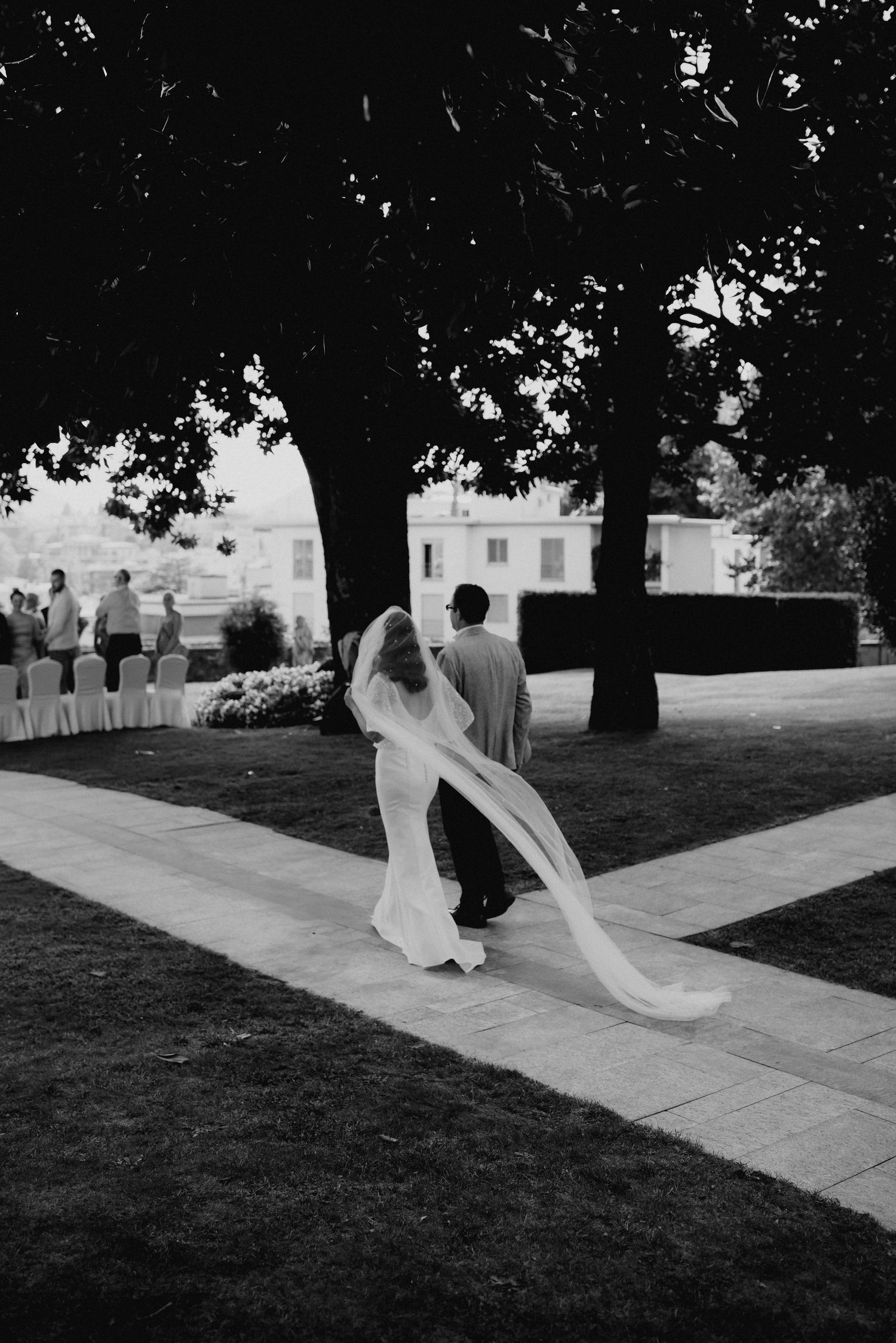 Black and white image of figures walking along a pathway under large trees at Villa Sassa Lugano.