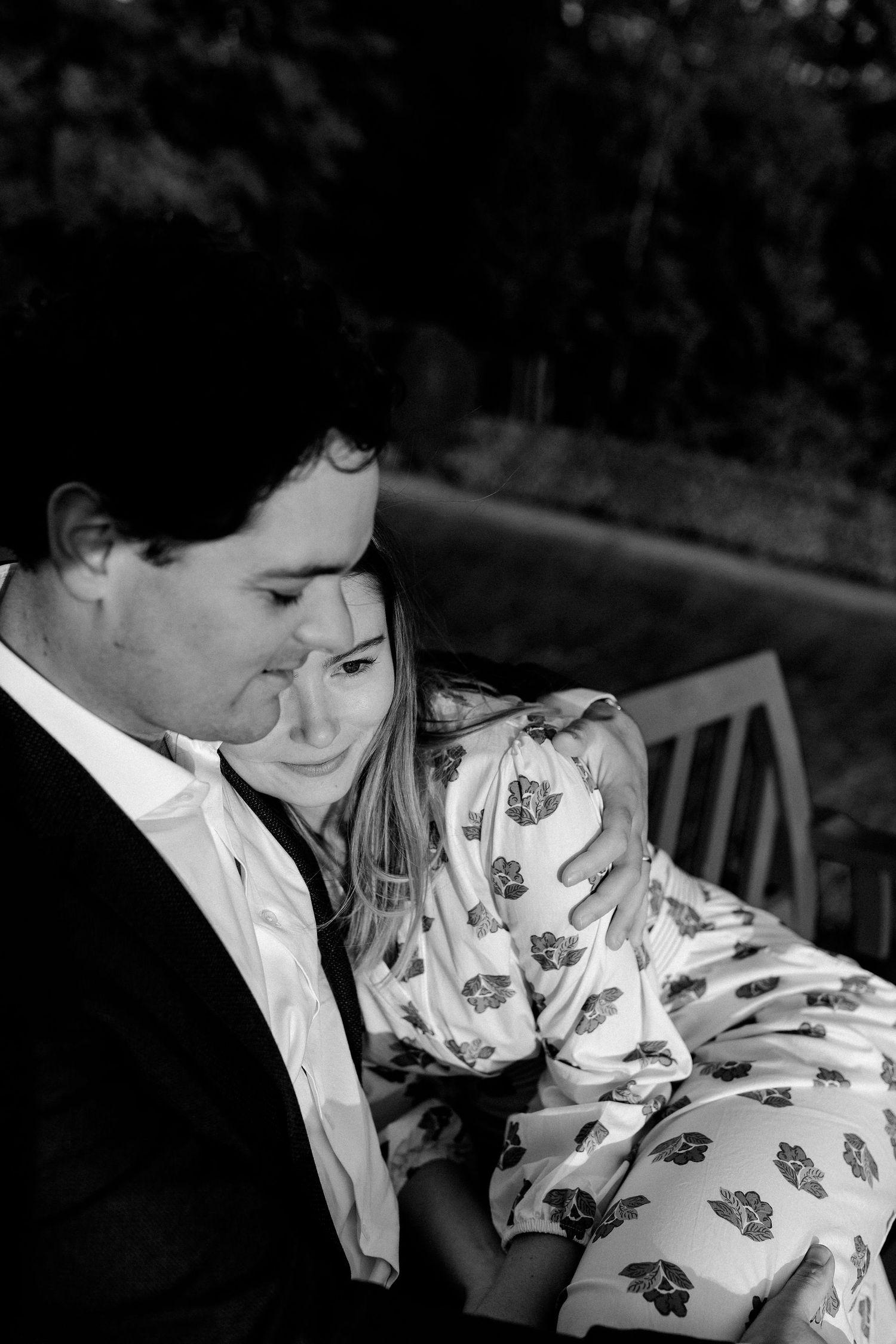 A tender black and white portrait of a couple sharing an intimate moment on a bench outdoors.