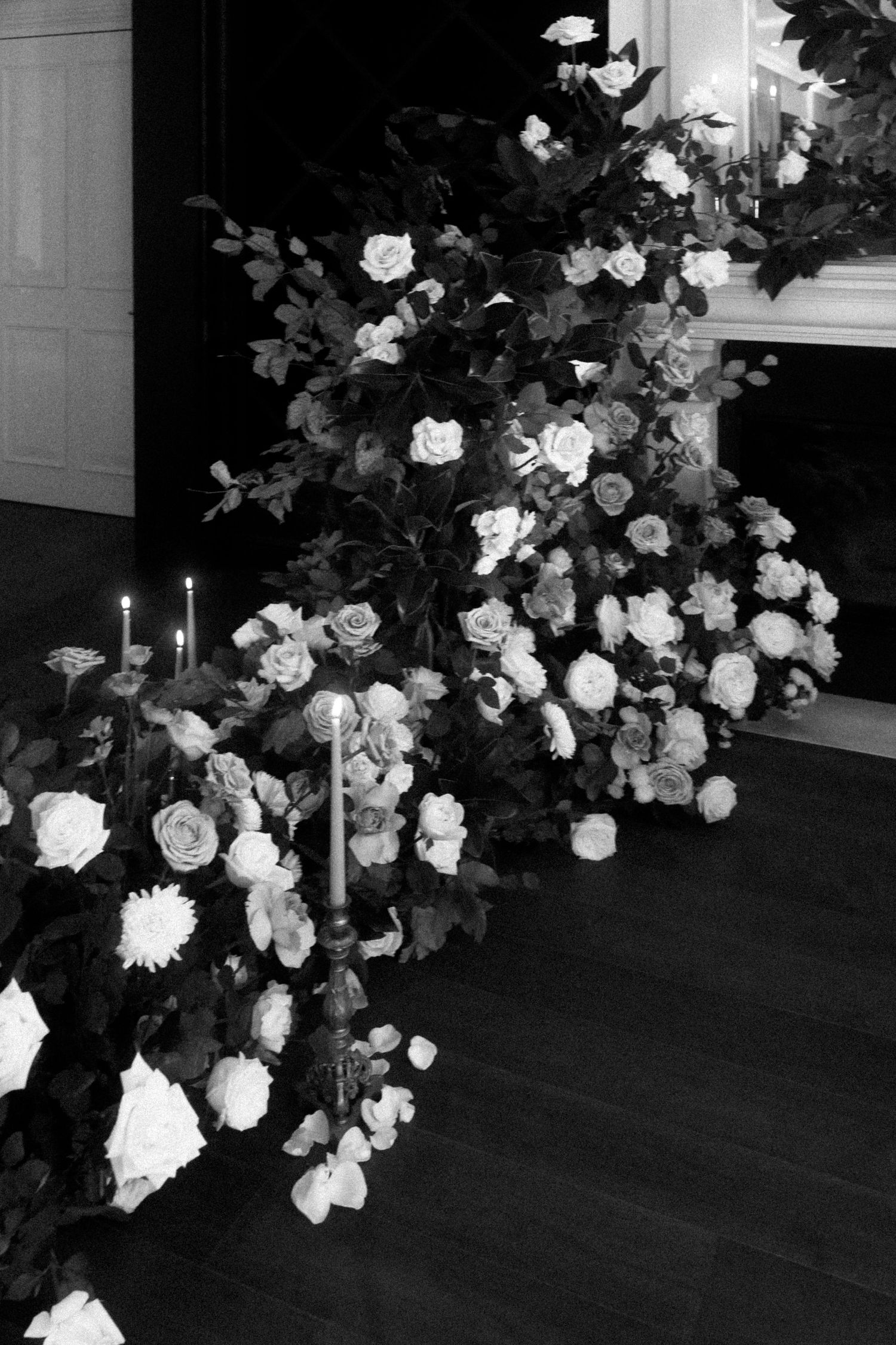 Black and white photo of an elegant floral arrangement with white roses and candles on a dark floor.