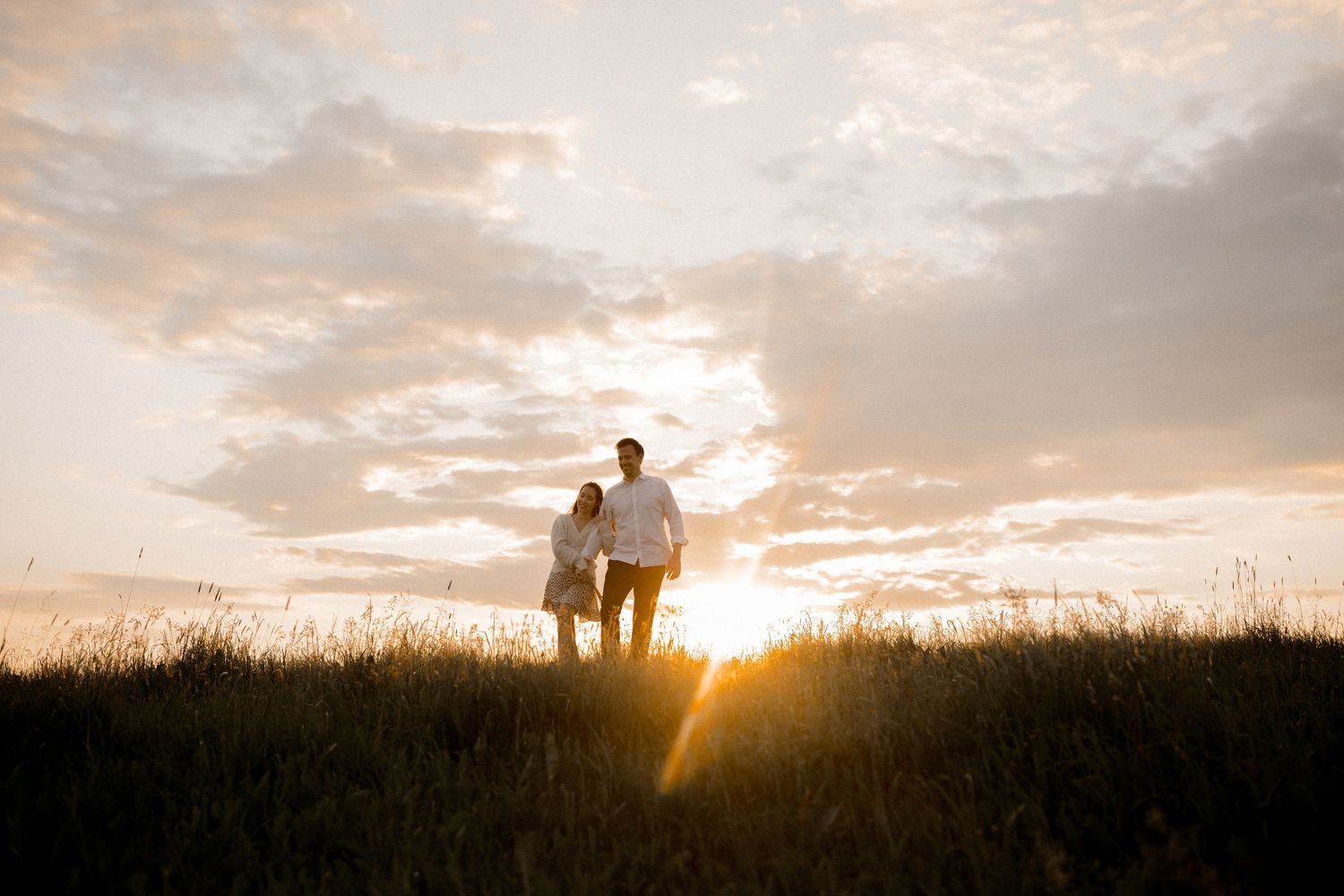 Silhouettes against a dramatic sunset sky in a grassy meadow.