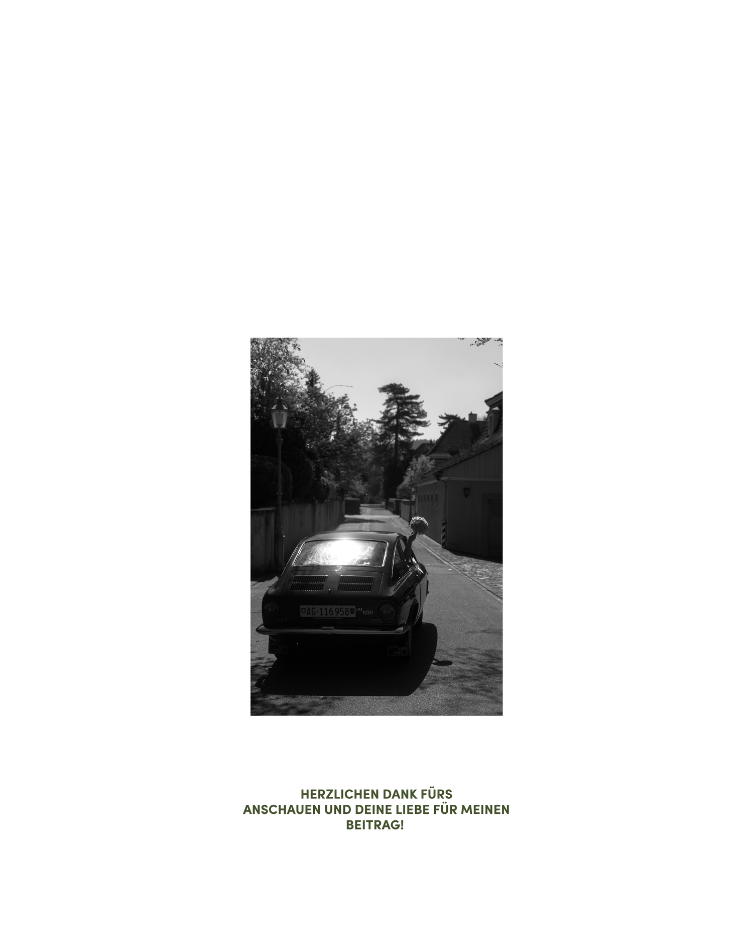 Black and white photo of a vintage car parked on a quiet tree-lined street with sunlight reflecting off its hood.